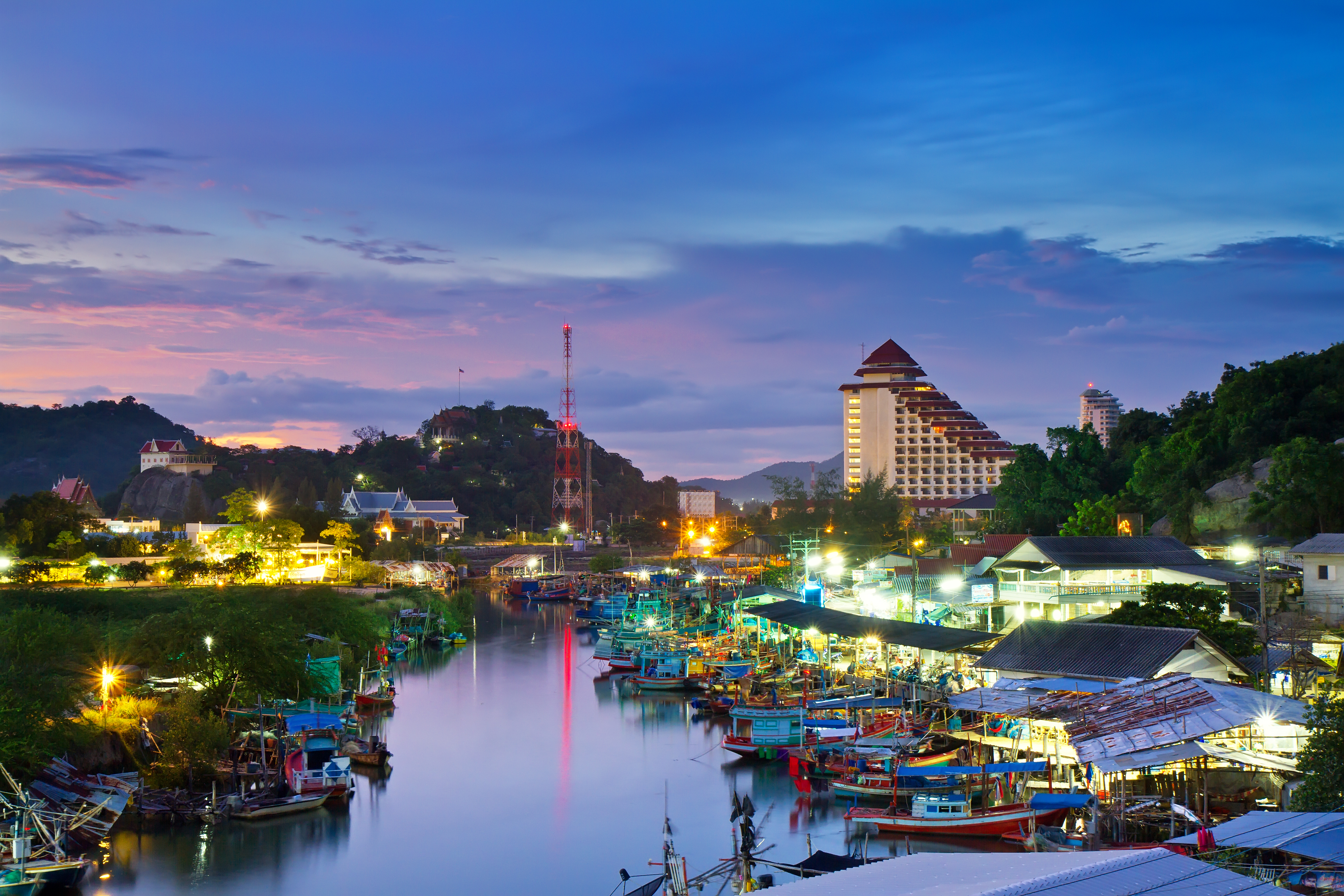 Smuk solnedgang over Hua Hin havn med farverige fiskerbåde og hotel i det fjerne