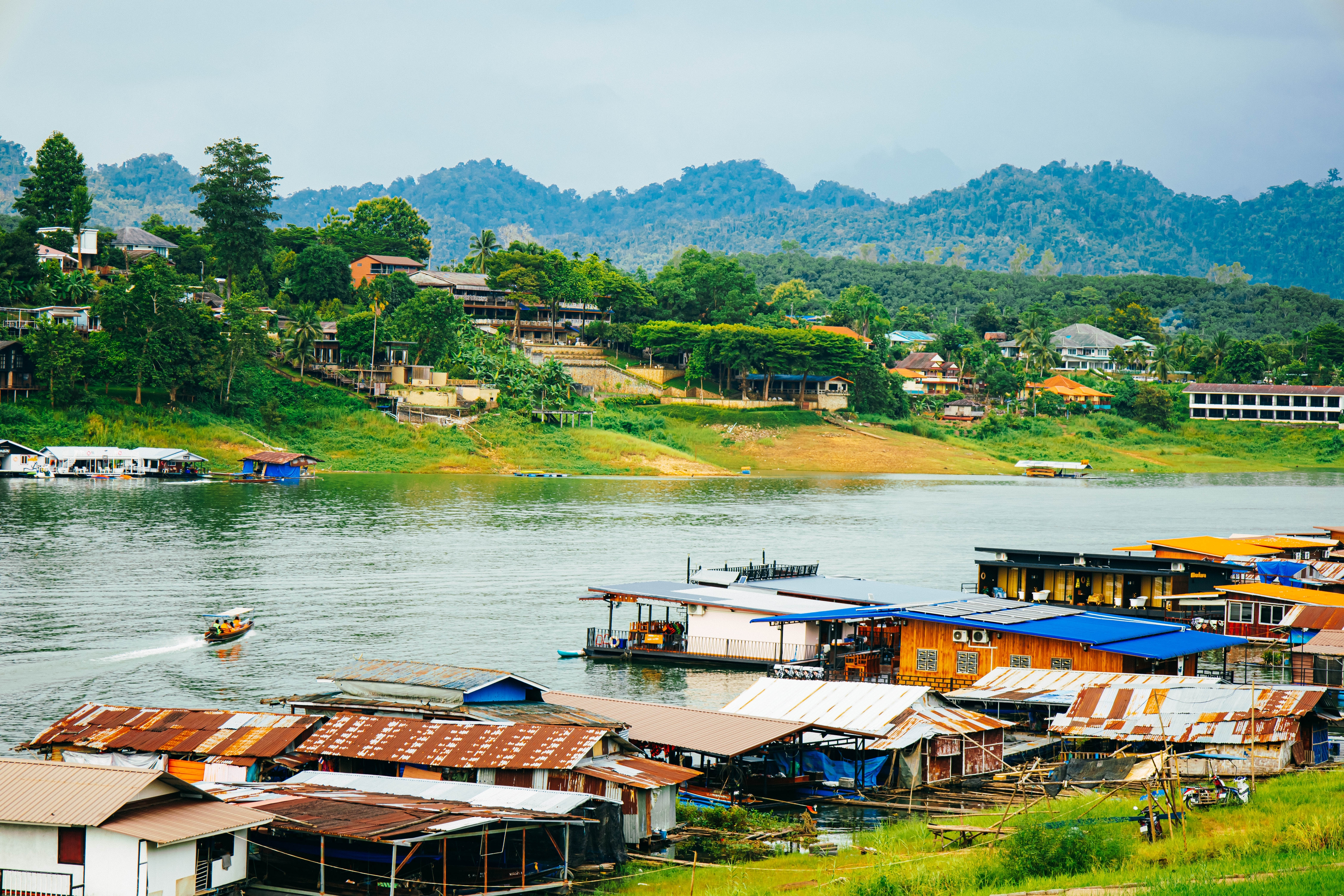 Stemningsfuld Mon-landsby ved bredden af floden i Kanchanaburi omgivet af grøn jungle og bjerglandskab i Thailand
