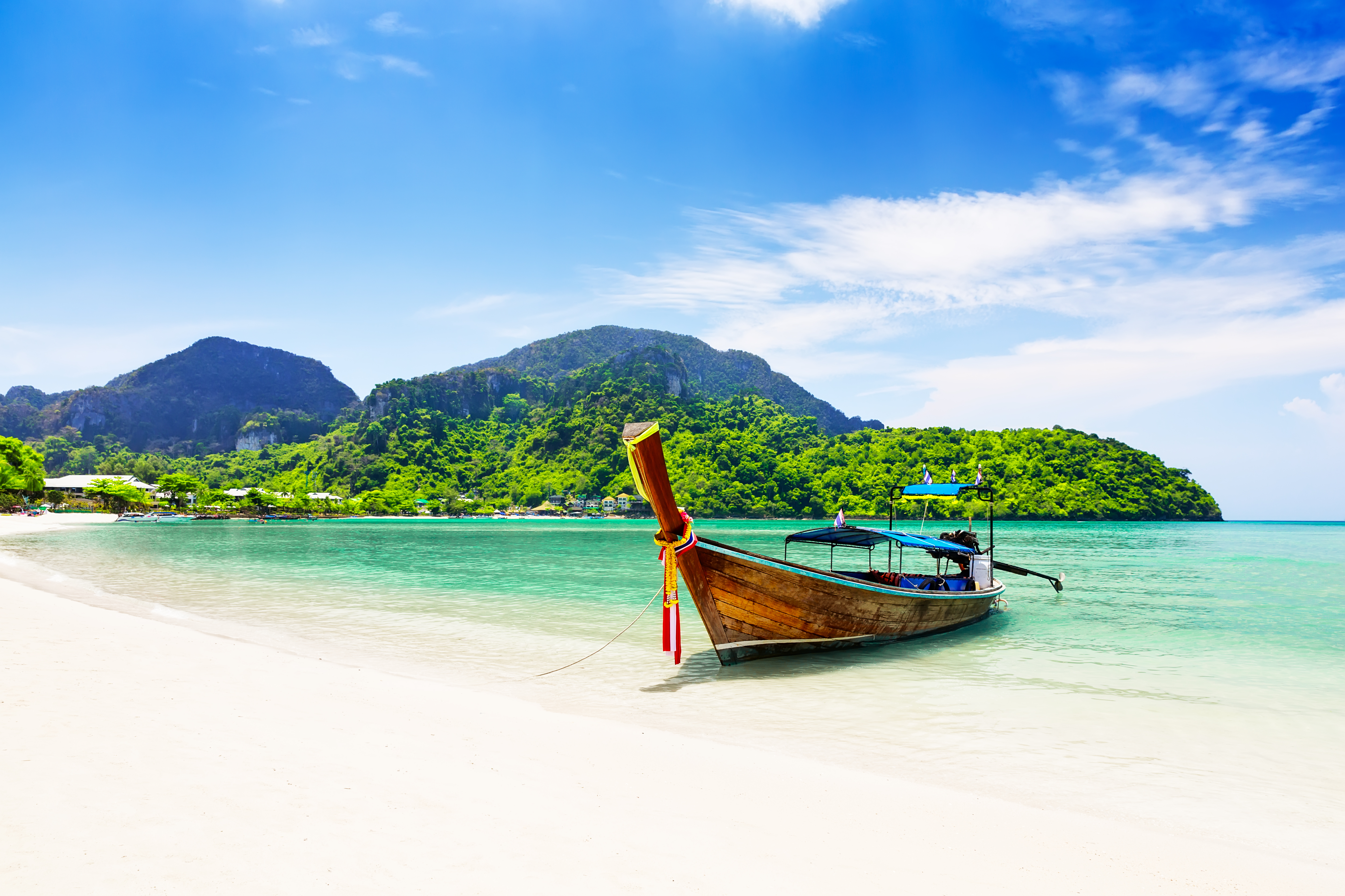 Paradisisk strand på thailandsk ø med longtail båd og krystalklart vand omgivet af jungle