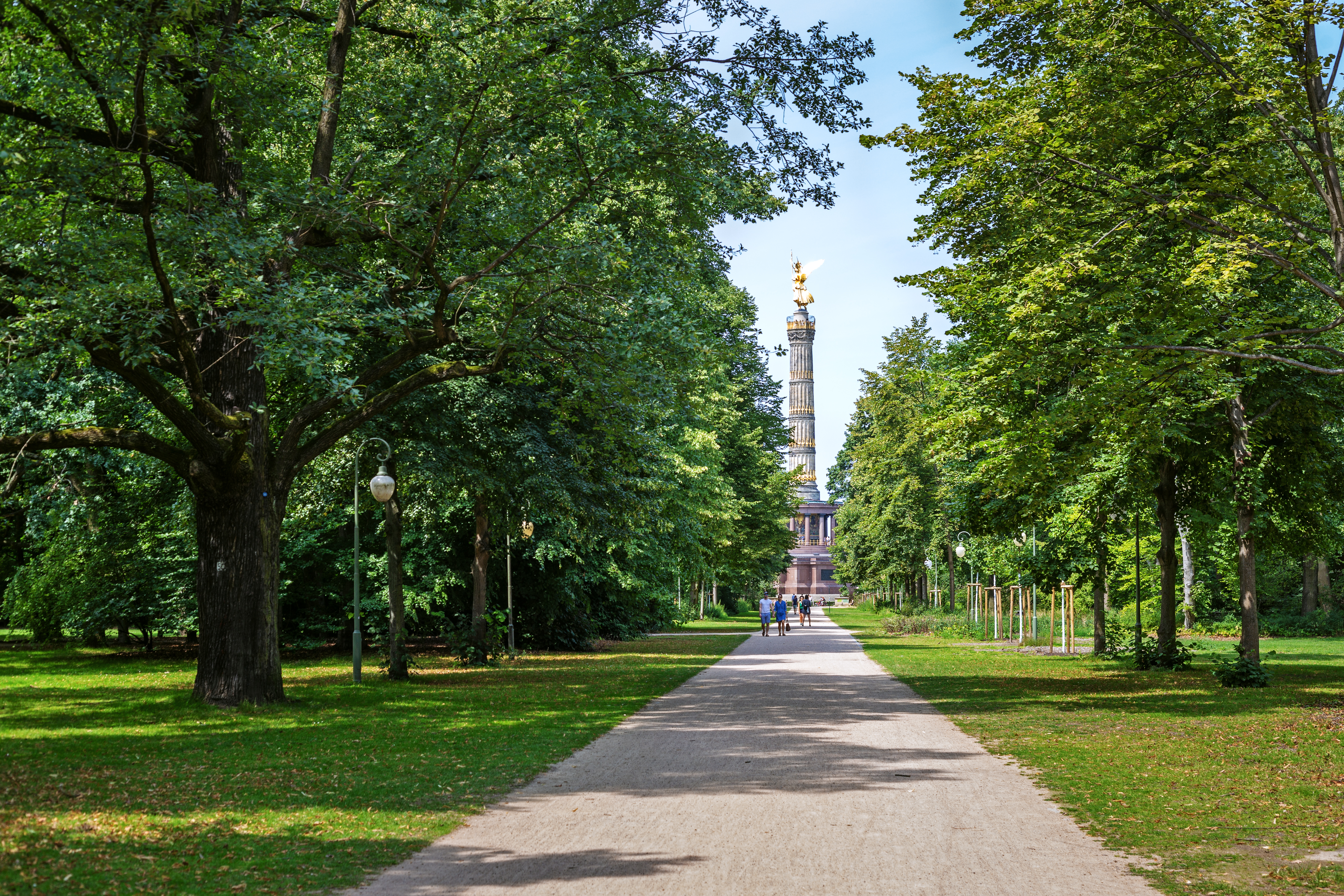 Grøn parkallé i Tiergarten i Berlin med den gyldne Sejrssøjle synlig mellem træerne om sommeren