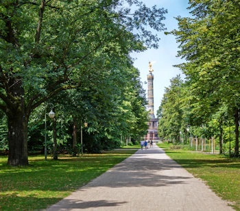 Grøn parkallé i Tiergarten i Berlin med den gyldne Sejrssøjle synlig mellem træerne om sommeren