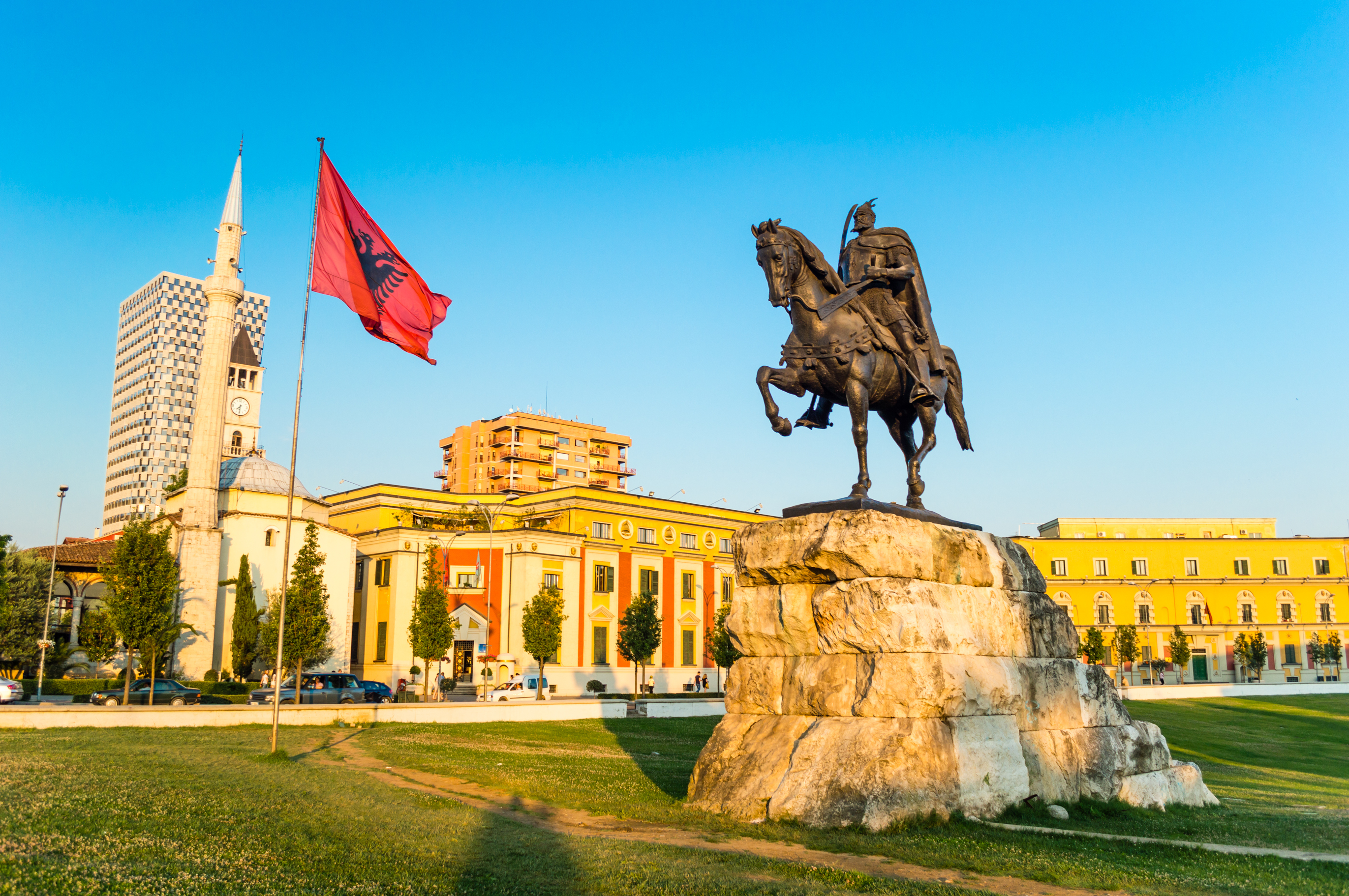 Bycentrum i Tirana med den ikoniske Skanderbeg-statue, det vajende albanske flag og den historiske Et'hem Bey-moske med dens karakteristiske minaret og grønne områder