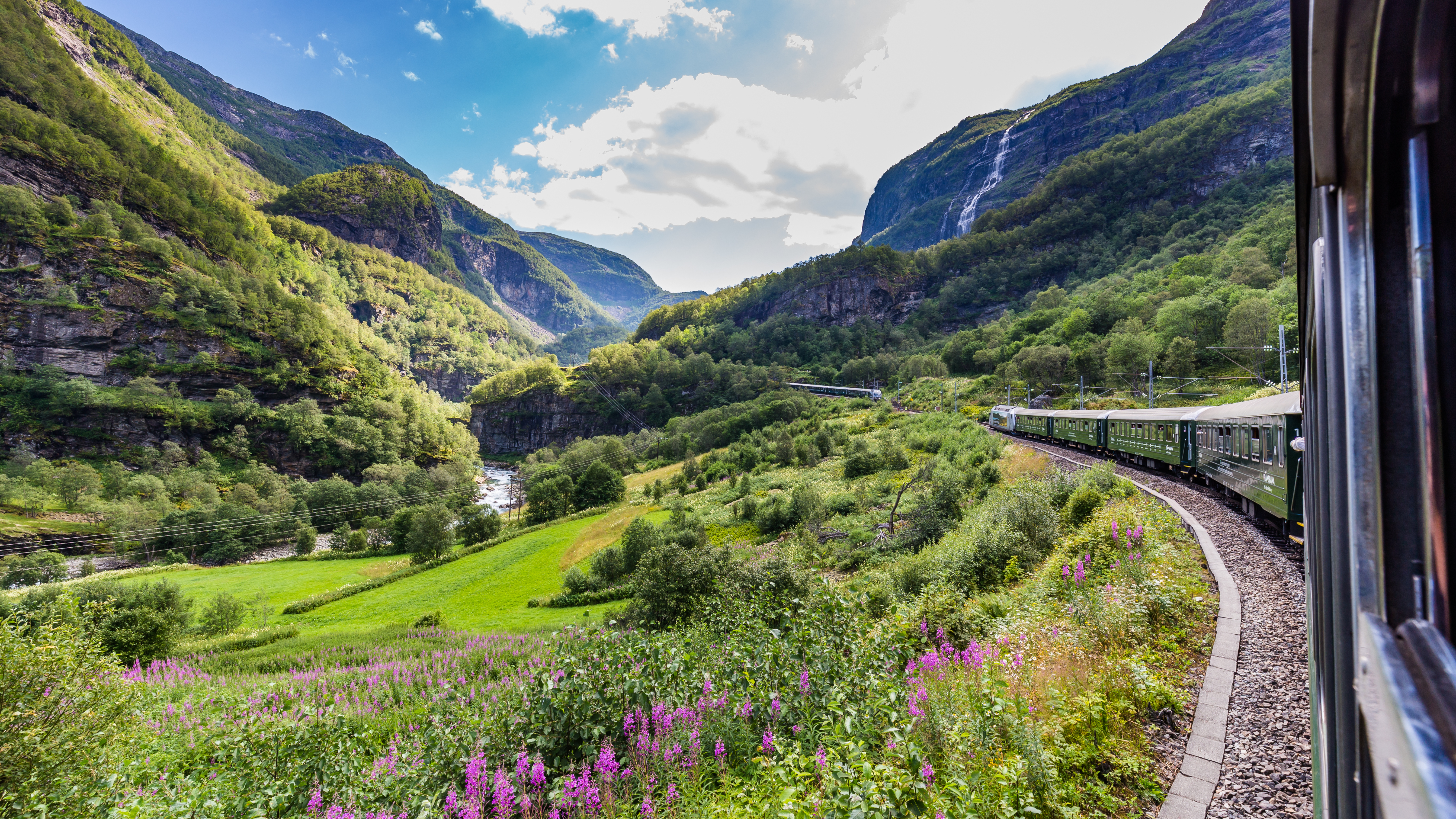 Storslået udsigt fra den berømte Flåmsbane, der strækker sig mellem Flåm og Myrdal i Aurland, med et fascinerende norsk landskab af stejle bjergsider, grønne skove og en glitrende flod