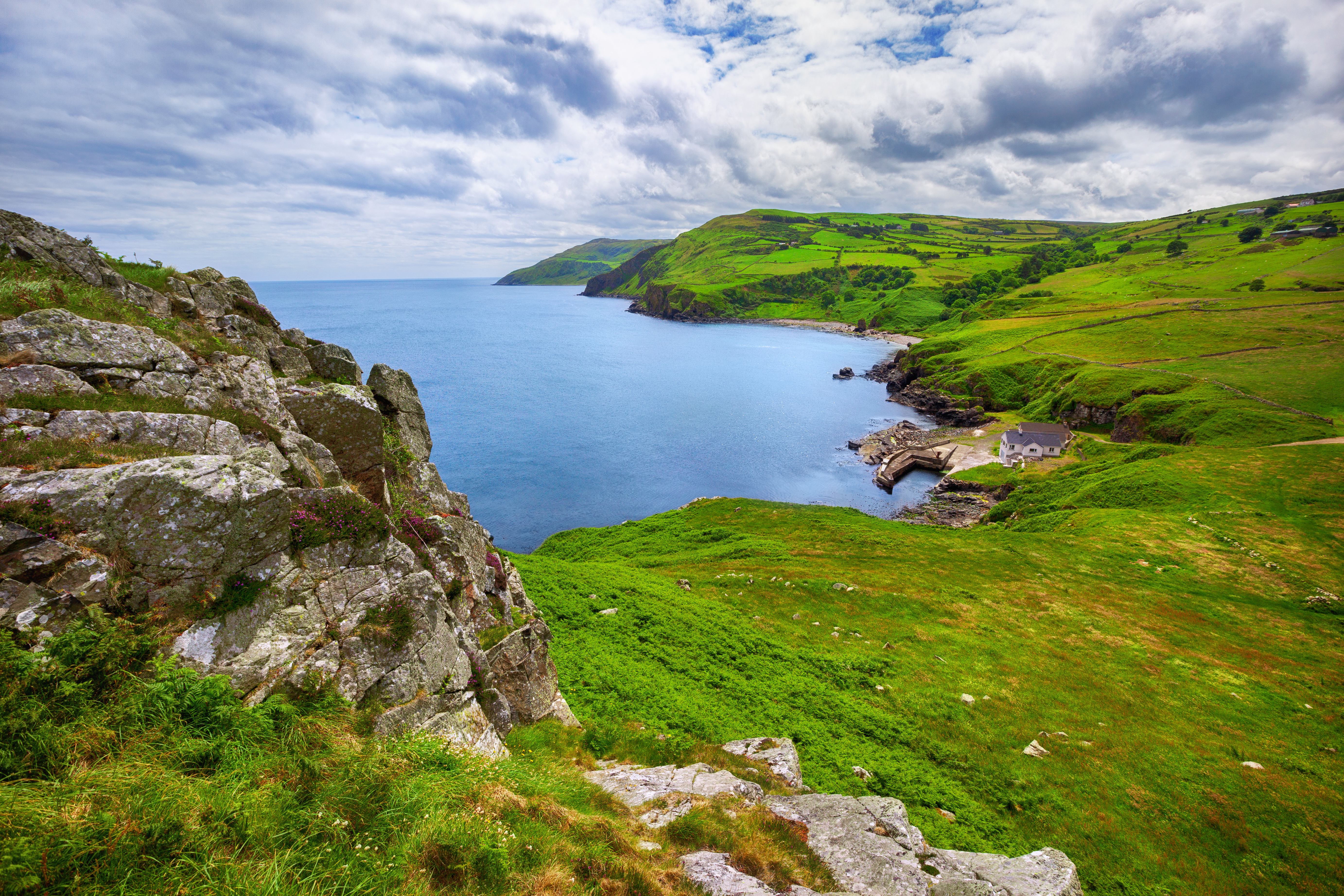 Idyllisk kystscene ved Torr Head i County Antrim, Nordirland, med frodige grønne bakker, markante klipper og udsigt over det rolige blå hav