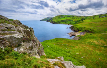 Idyllisk kystscene ved Torr Head i County Antrim, Nordirland, med frodige grønne bakker, markante klipper og udsigt over det rolige blå hav