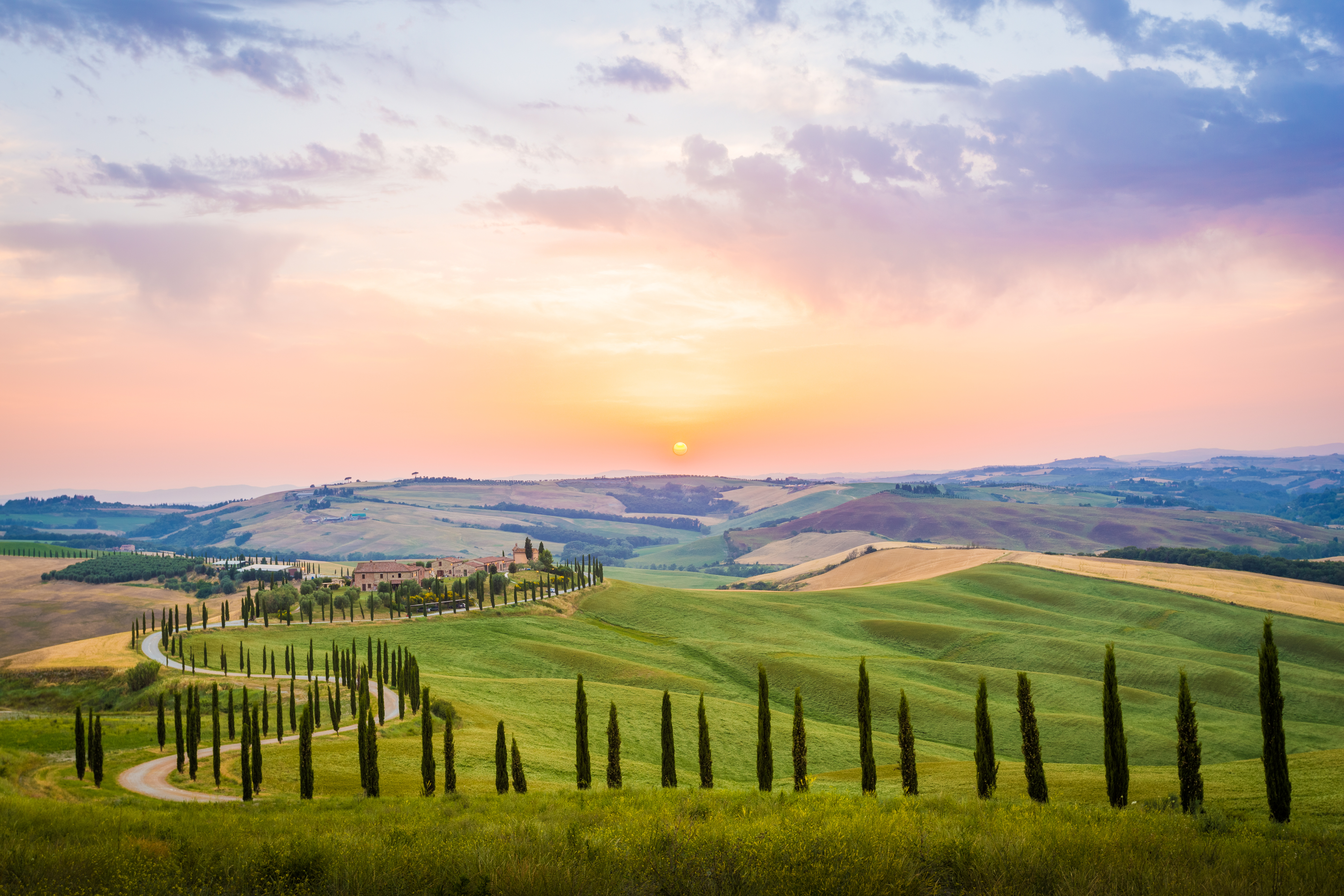 Charmerende landsted med cypresser og oliventræer i det bølgende landskab ved solopgang i Crete Senesi, Toscana