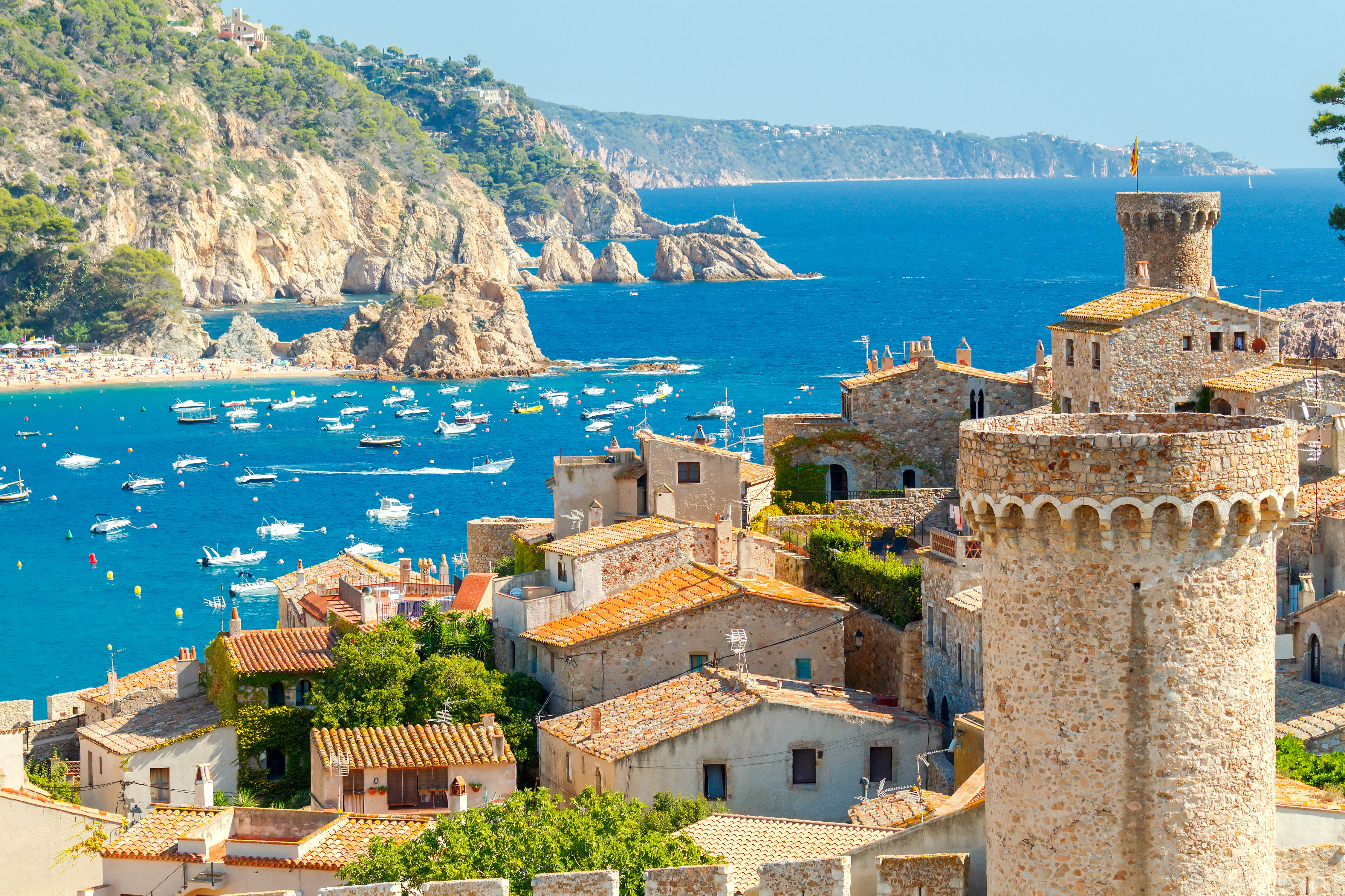 Charmerende udsigt over Tossa de Mar med historiske middelalderlige tårne og bymure, spanske stenhuse og en smuk turkisblå bugt på Costa Brava