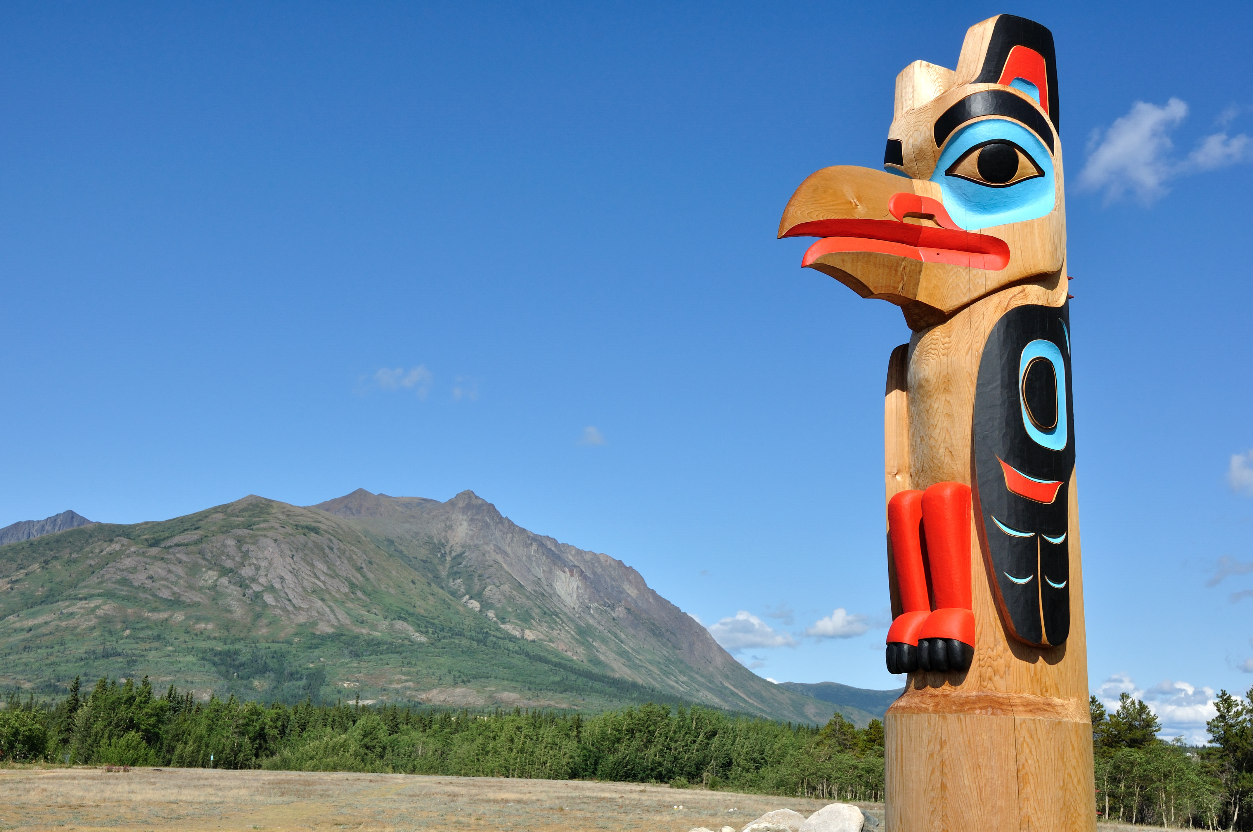 Traditionel håndskåret totempæl med ørn og indianske mønstre i rødt, sort og turkis i Carcross, Yukon