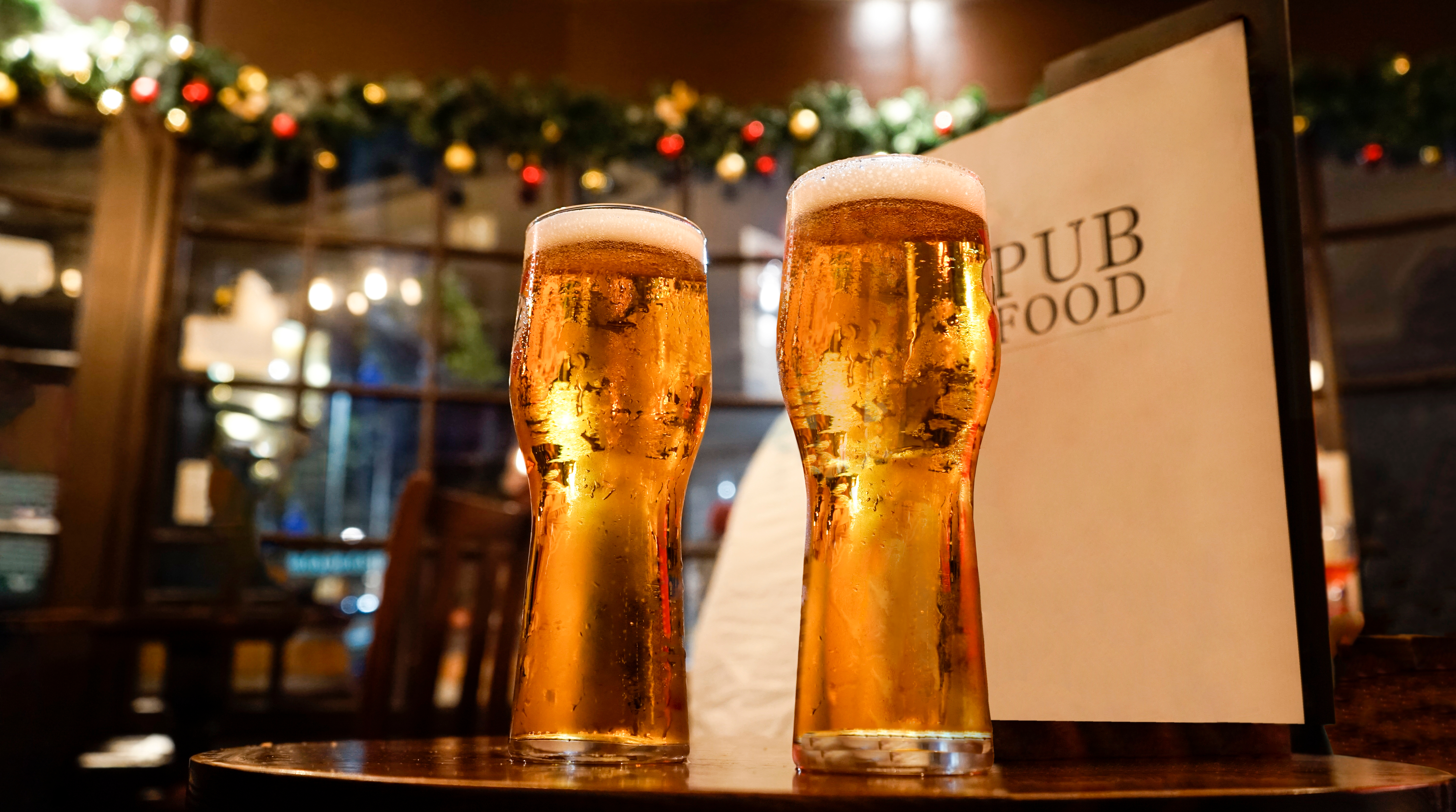 To kolde glas øl i en traditionel engelsk pub i London med juledekoration og pub food menu på bordet