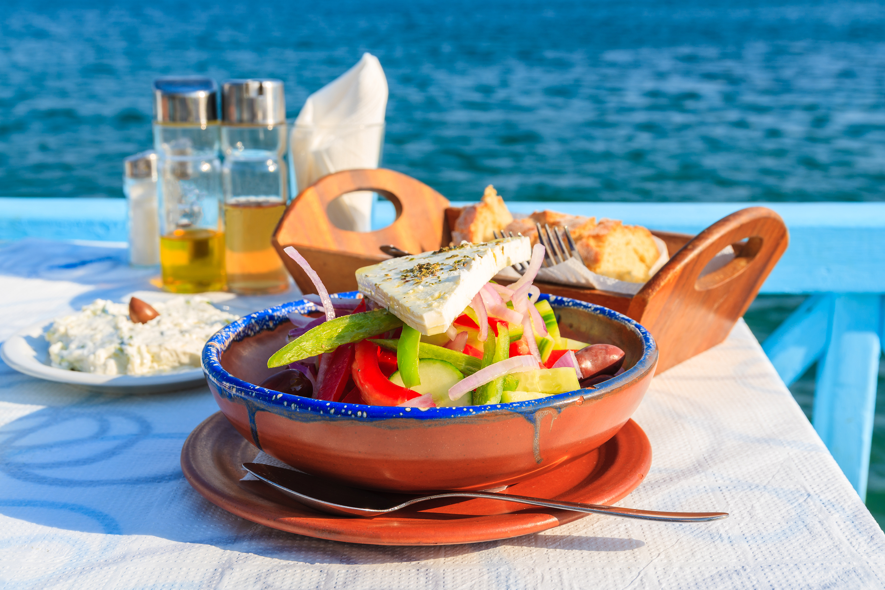 Frisk græsk salat med agurk tomat og feta serveret på solrig terrasse med havudsigt