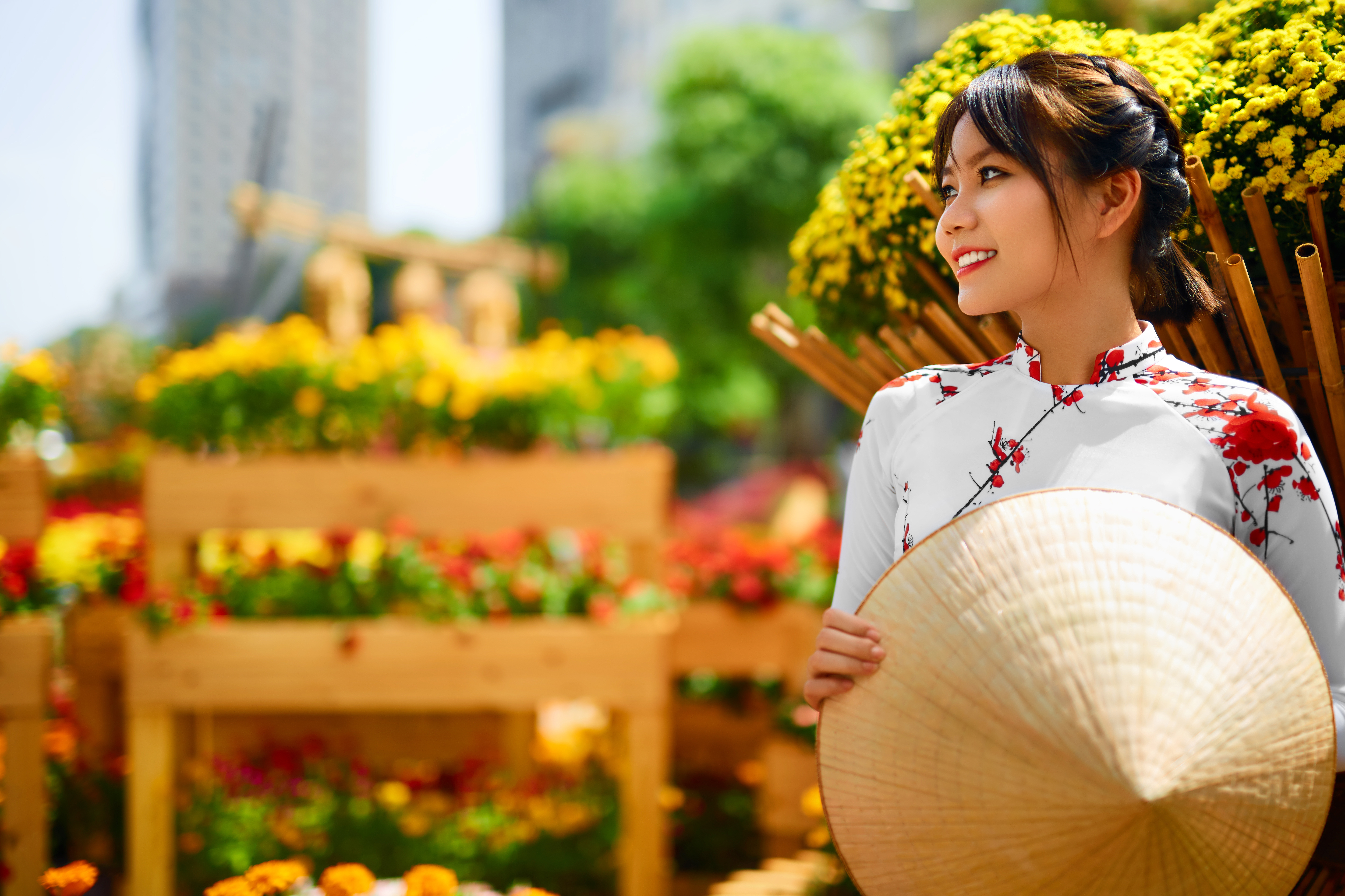 Glad vietnamesisk kvinde klædt i traditionel Ao Dai og Non La hat blandt farverige blomster i Vietnam