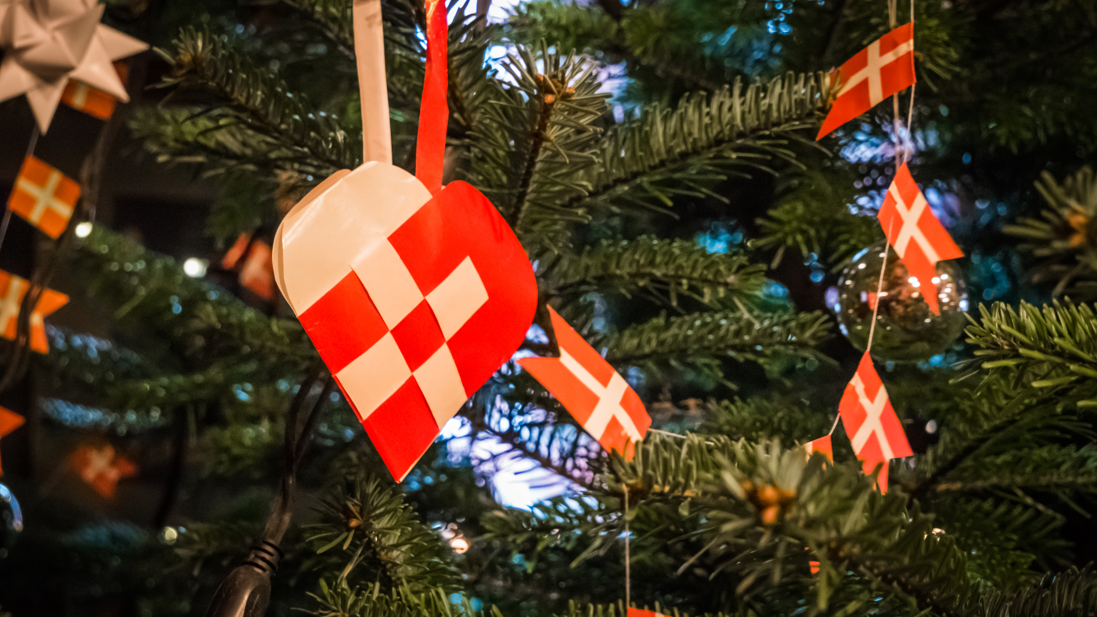 Traditionel dansk julepynt med flettede papir-julehjerter i rødt og hvidt prydet med små Dannebrogsflag på et grønt juletræ - oplev den ægte danske julehygge med Nille Rejsers julerejser