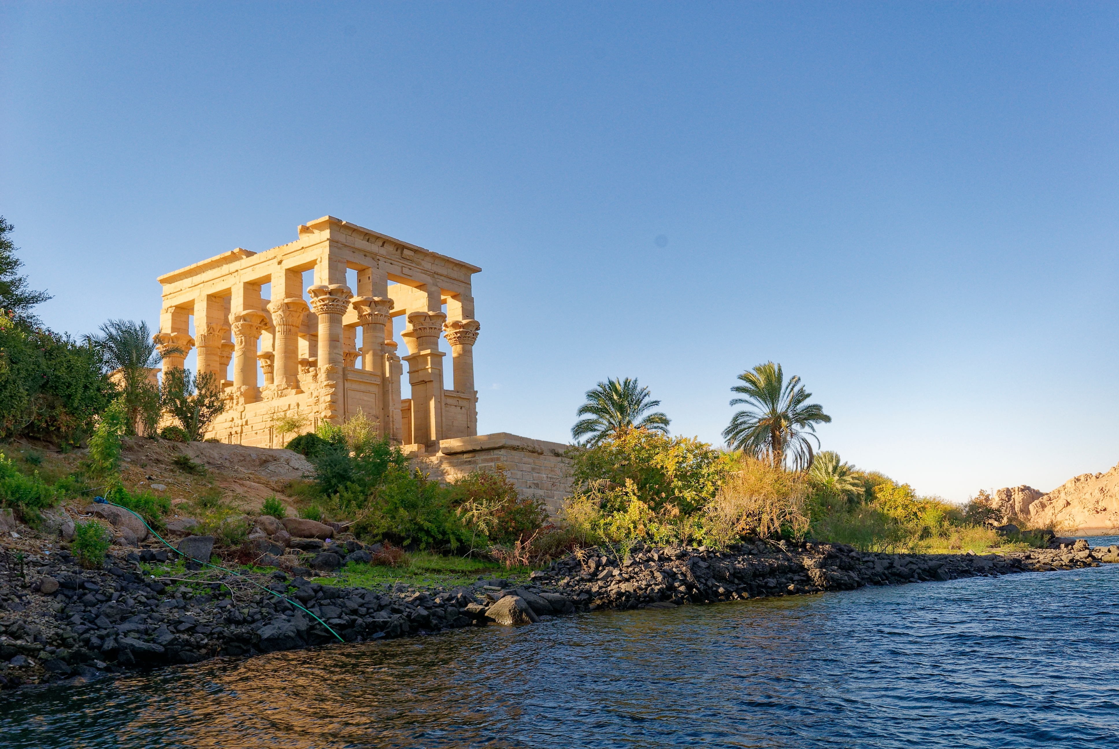 Antik Trajans Kiosk ved Philae Templet på Nilens bredder i Egypten, omgivet af frodig natur og blåt vand