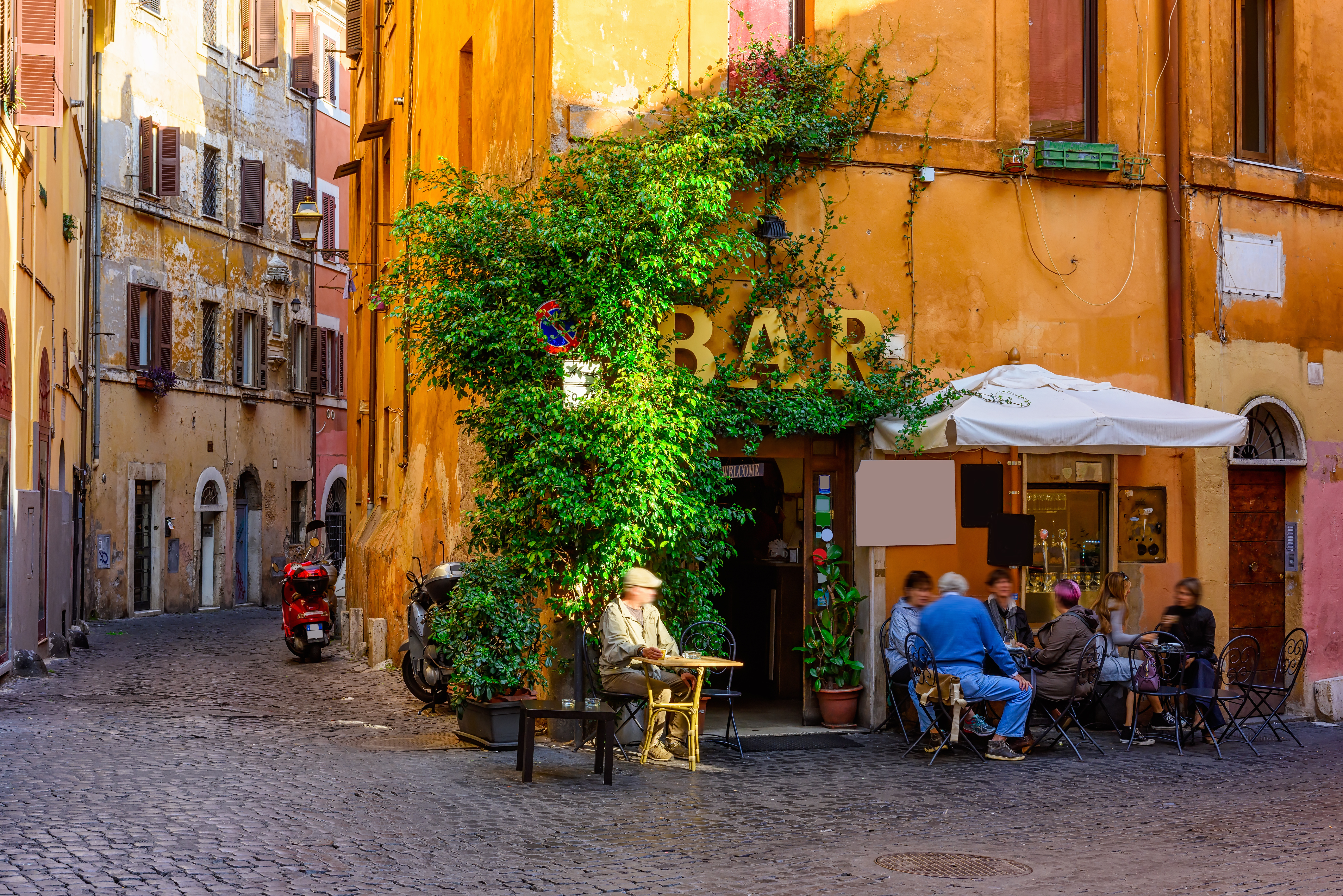 Romantisk smal gade i Trastevere-distriktet i Rom med farverige bygninger, en intim udendørs café og frodige planter, der indfanger den særlige romerske stemning i et af byens mest karakteristiske kvarterer
