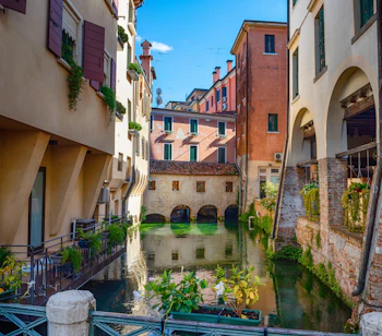 Charmerende kanal i Treviso, Veneto, omgivet af historiske italienske bygninger med farverige facader og frodig vegetation på en solskinsdag