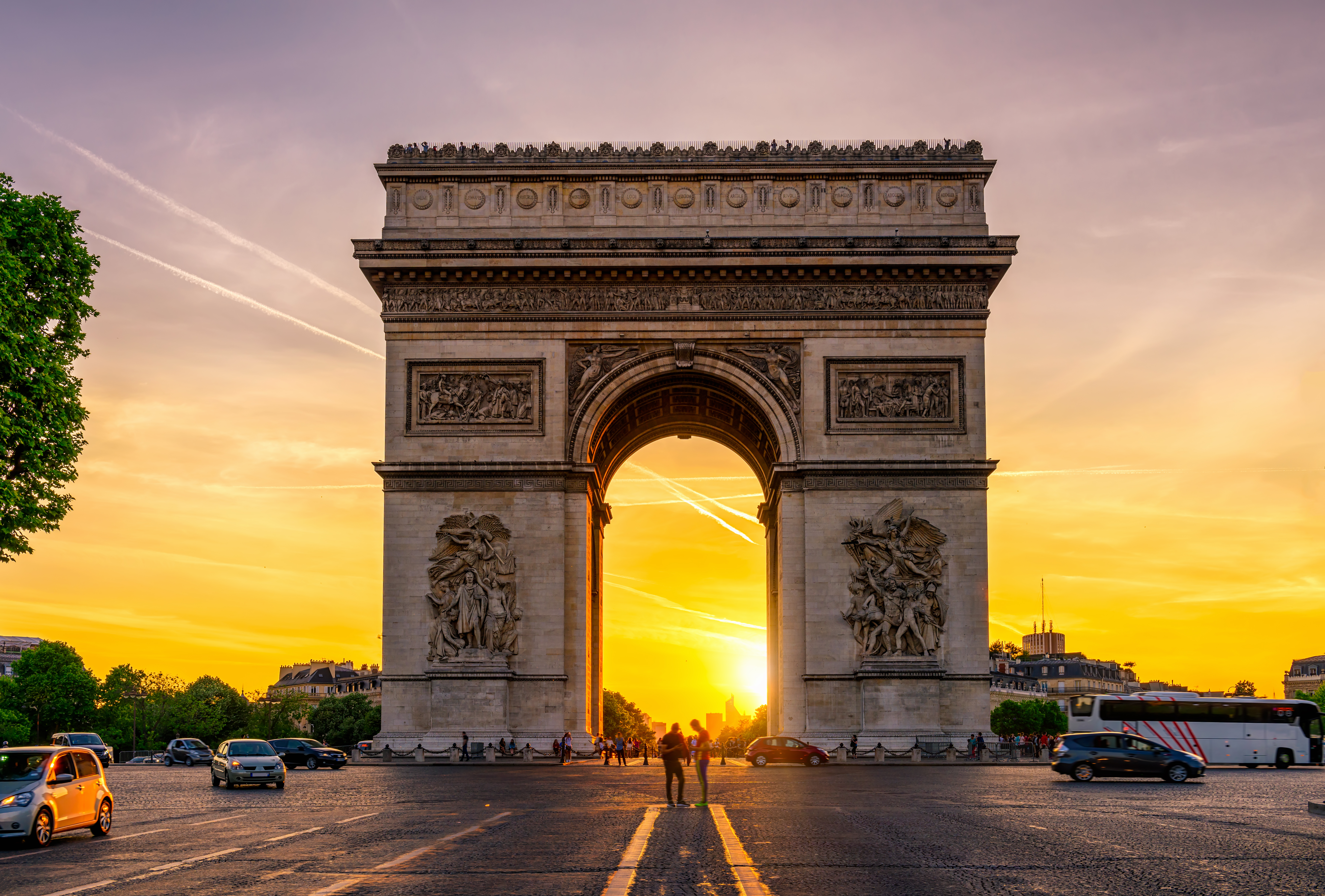 Triumfbuen i Paris ved solnedgang med orange himmel og Champs-Elysées boulevard