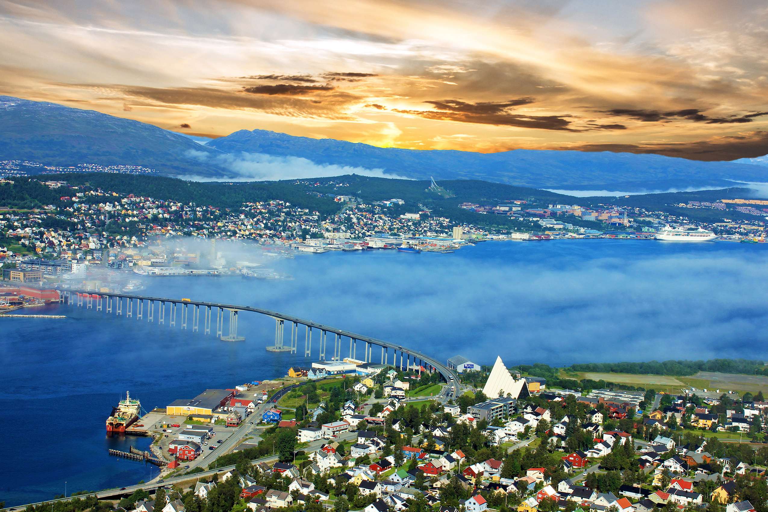 Spektakulær udsigt over Tromsø i Norge med broen over fjorden, tåge over vandet og smukke bjerge i baggrunden ved solnedgang
