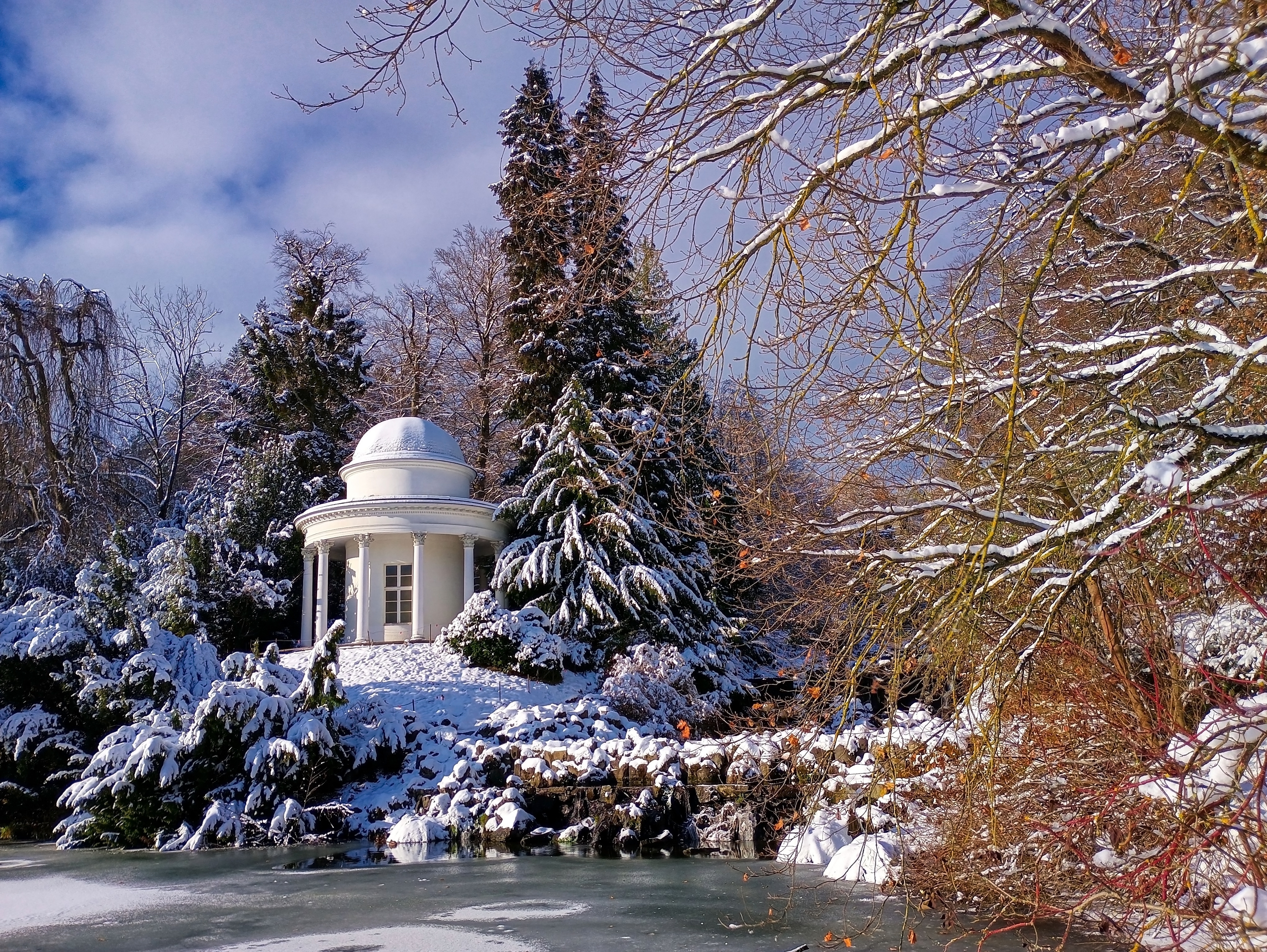 Eventyrligt vinterlandskab med hvidt tempel i Bergpark Wilhelmshöhe, Kassel, Hessen med snedækkede træer og frossen sø