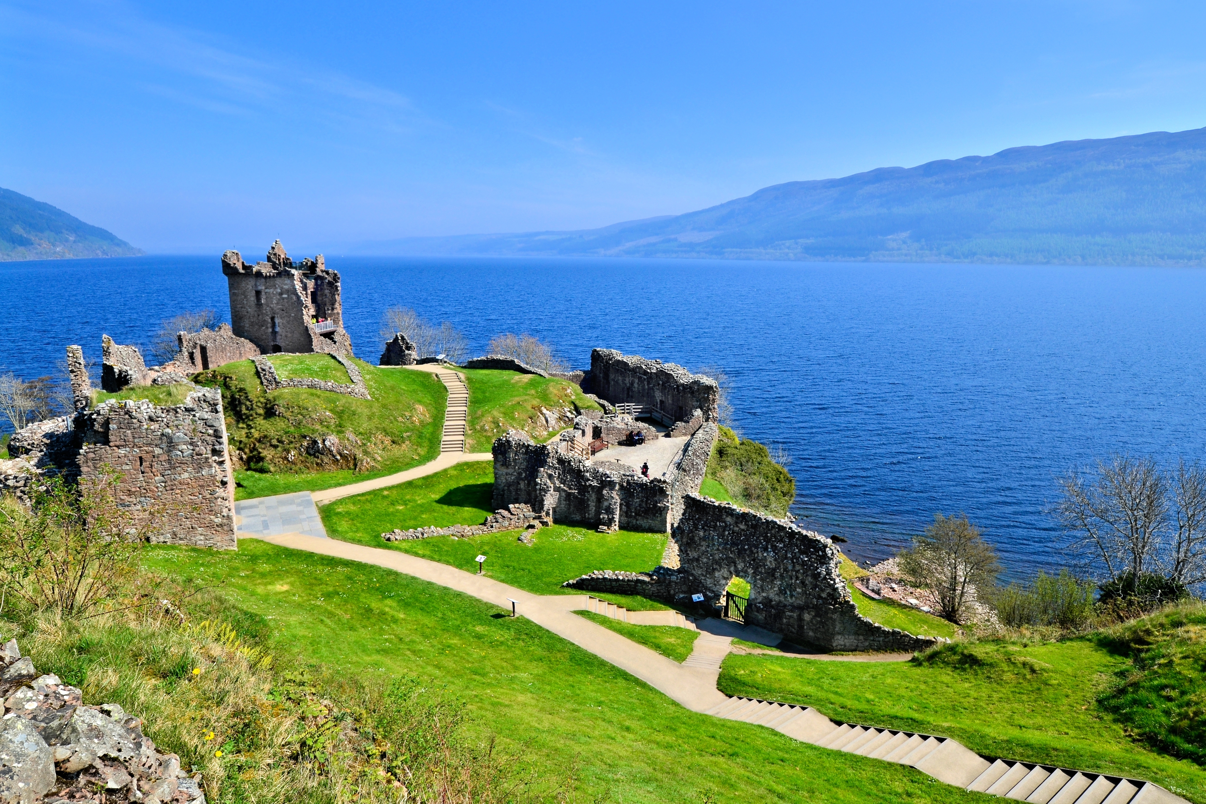De imponerende stenruiner af det historiske Urquhart Castle med smukke grønne omgivelser og den ikoniske Loch Ness sø i det skotske højland