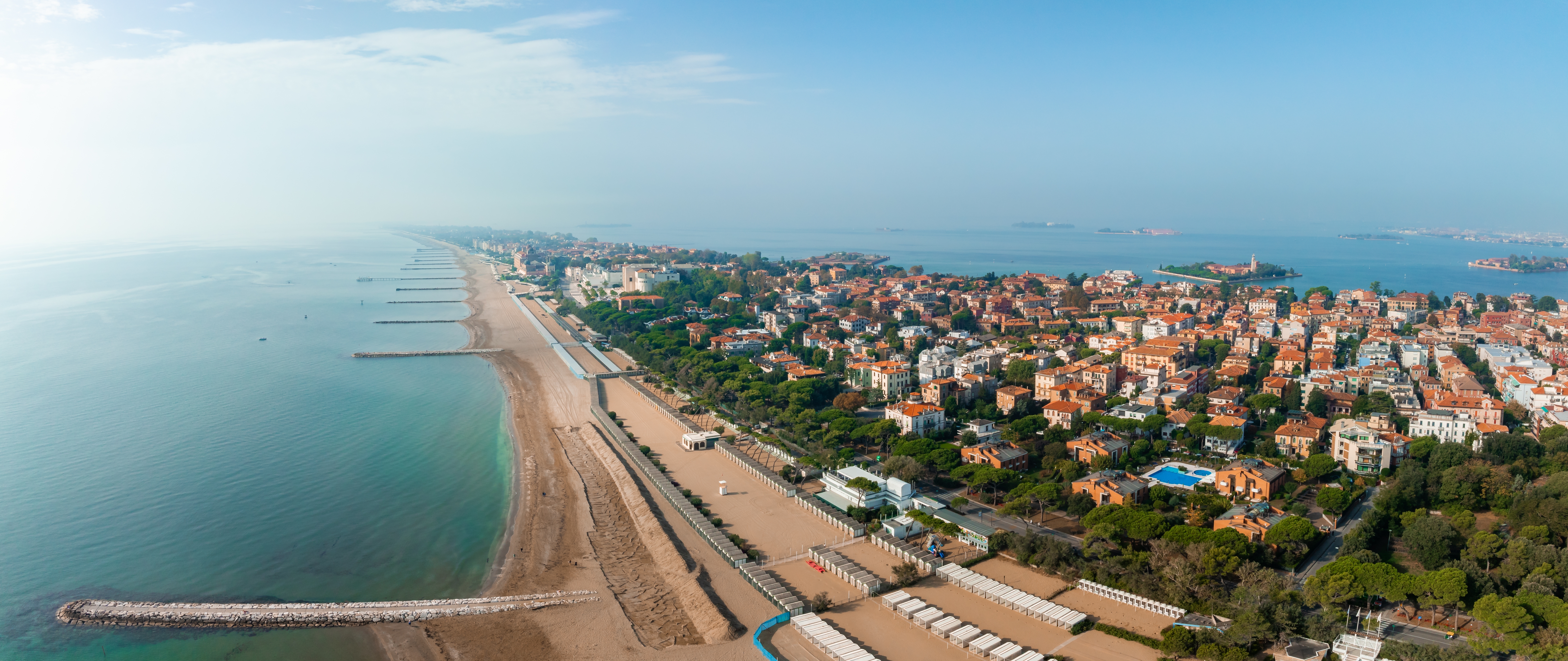 Smukt luftfoto af Lido di Venezia med lang sandstrand, grønne træer og udsigt over Venedigs lagune, Italien