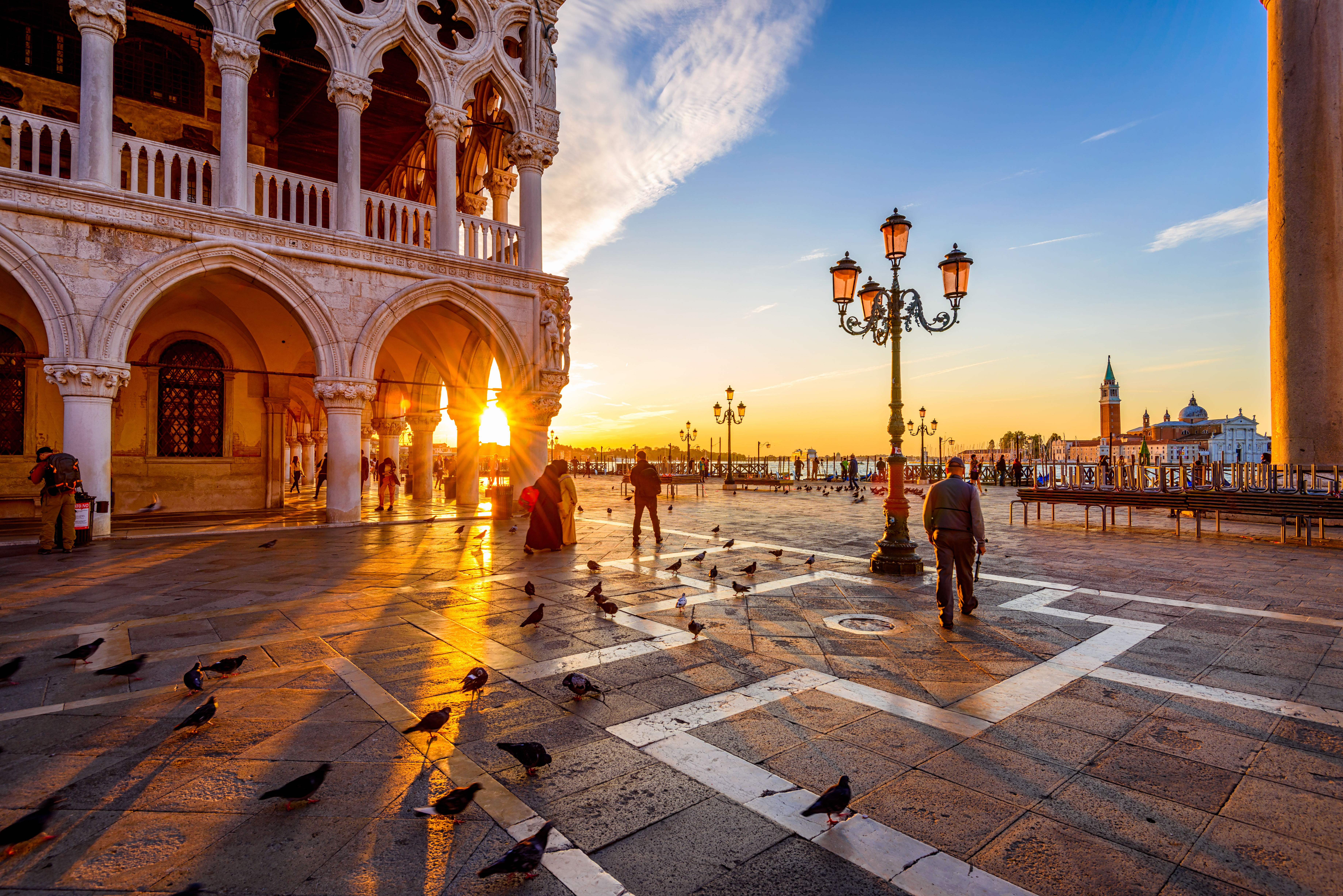 Idyllisk morgenstemning på Markuspladsen i Venedig med det historiske Dogepalads badet i gyldent solopgangslys og de karakteristiske søjler