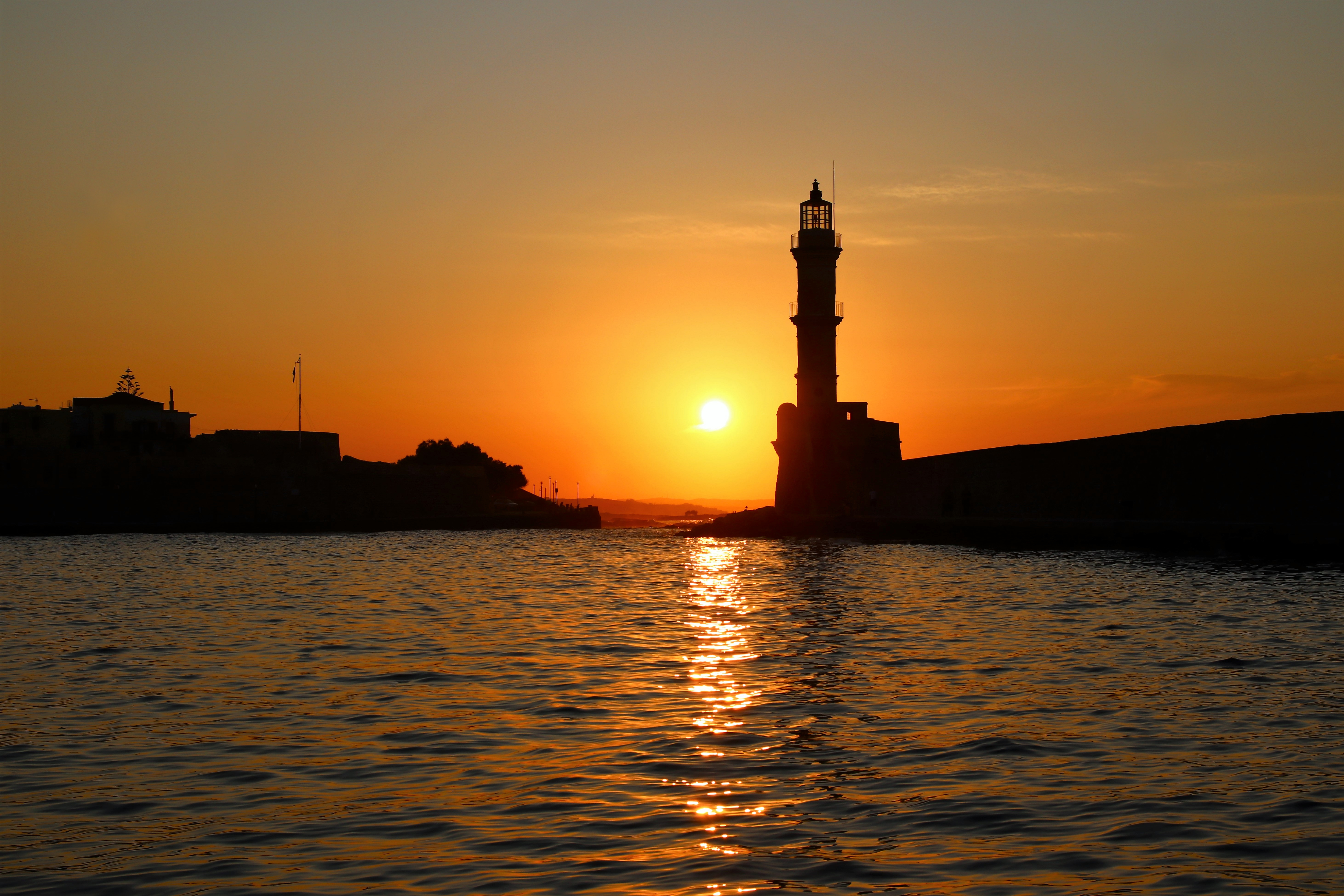 Det smukke venetianske fyrtårn i Chania på Kreta fotograferet ved solnedgang med gyldent lys reflekteret i havnens vand