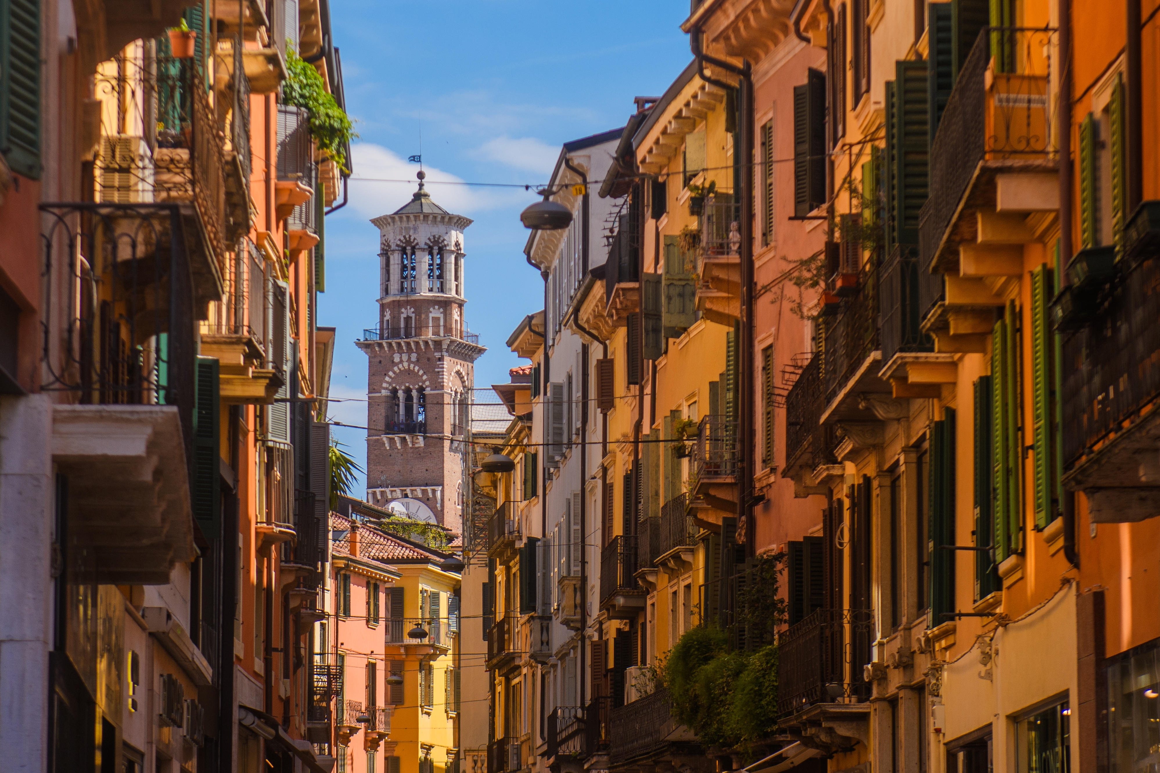 Pittoresk gadescene i Verona med farverige bygninger i orange og rosa nuancer, grønne skodder og balkoner samt det historiske klokketårn Torre dei Lamberti