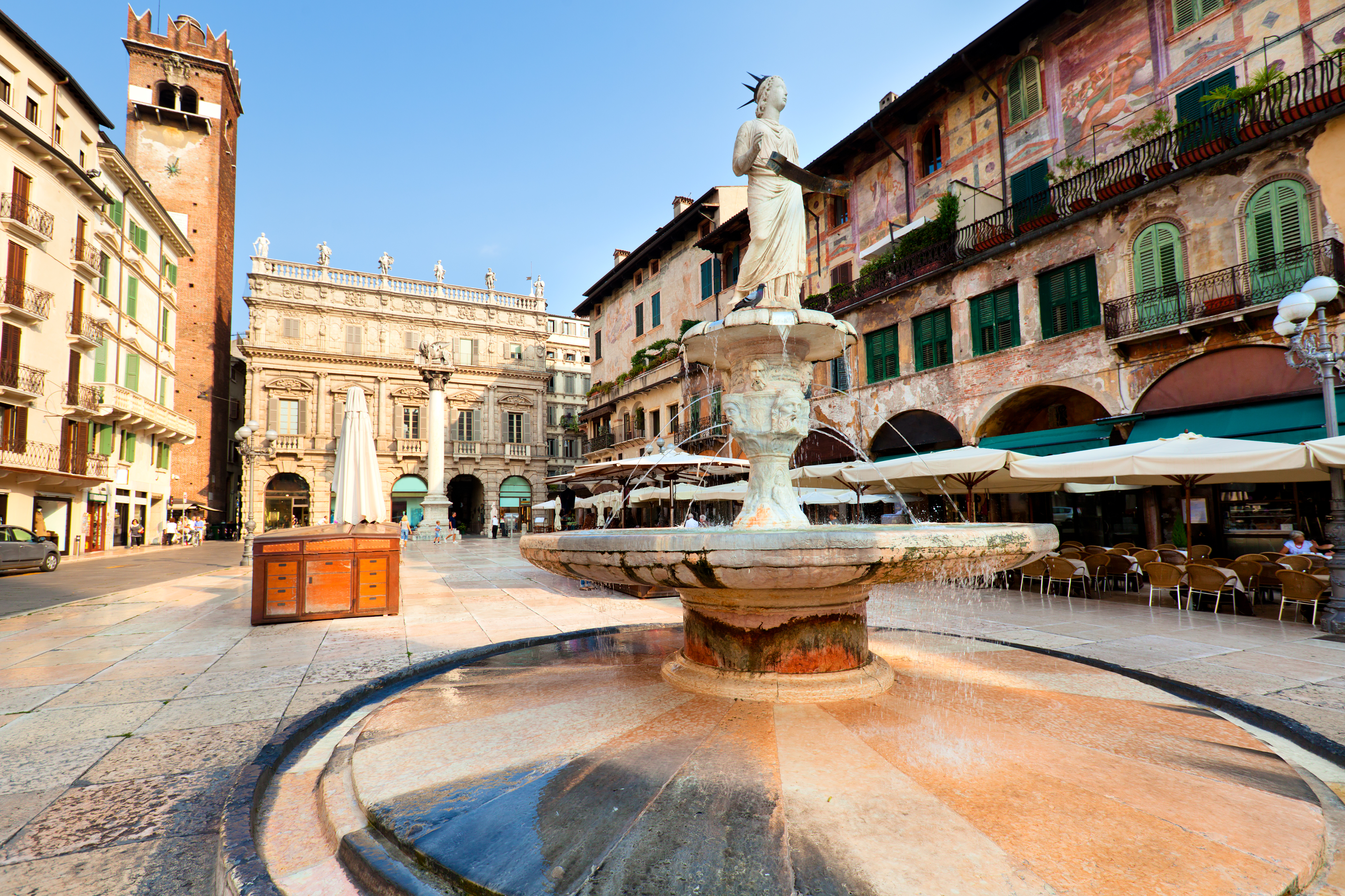 Stemningsfuldt morgenlys over Piazza delle Erbe i Verona med ikoniske skulpturer, fontæner og middelalderlig arkitektur