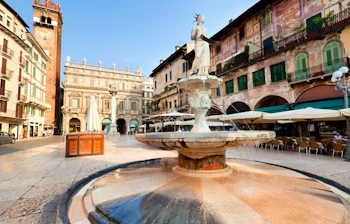Stemningsfuldt morgenlys over Piazza delle Erbe i Verona med ikoniske skulpturer, fontæner og middelalderlig arkitektur
