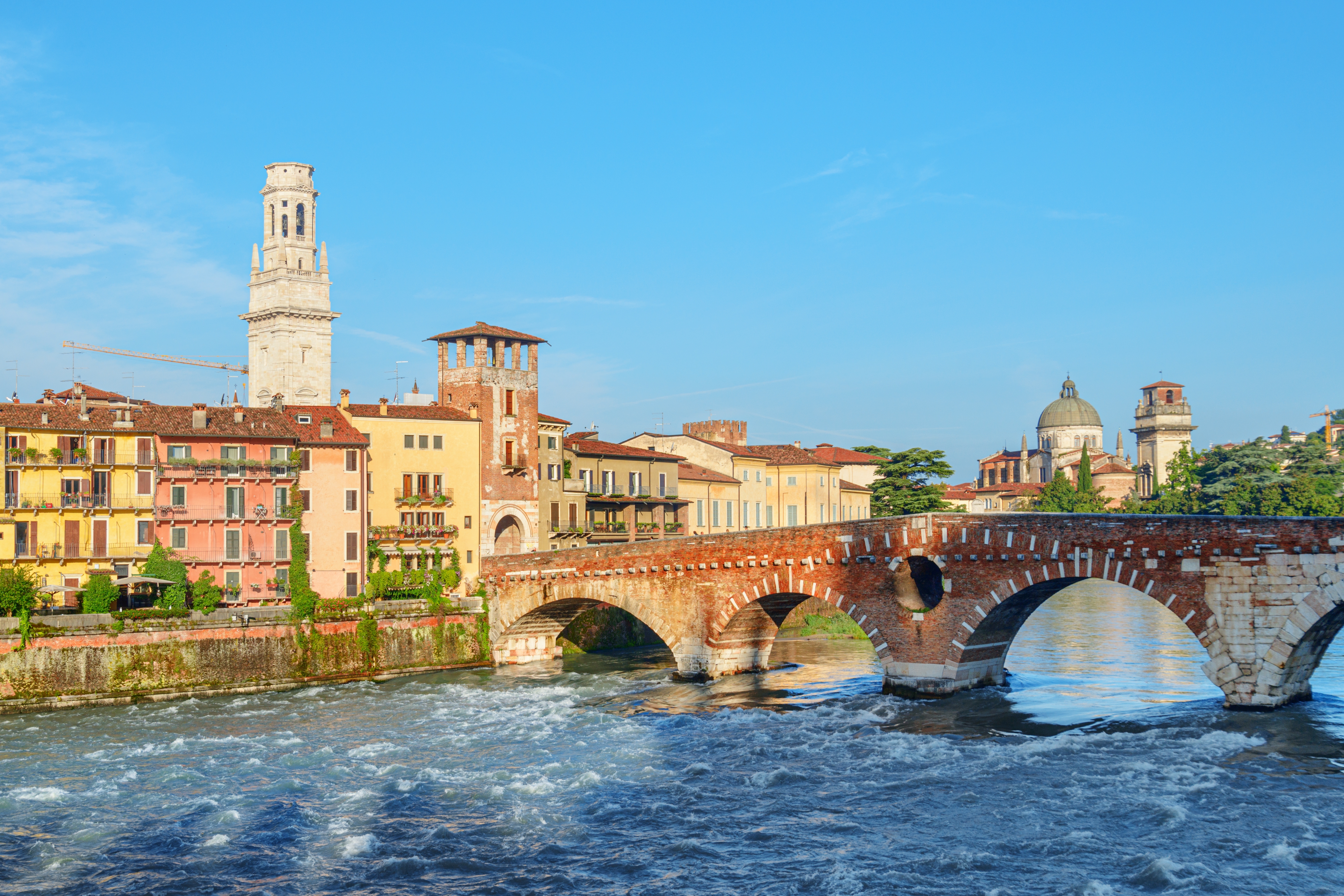 Udsigt over Ponte Pietra-broen og Adige-floden i Verona med middelalderlige tårne og farverige italienske bygninger
