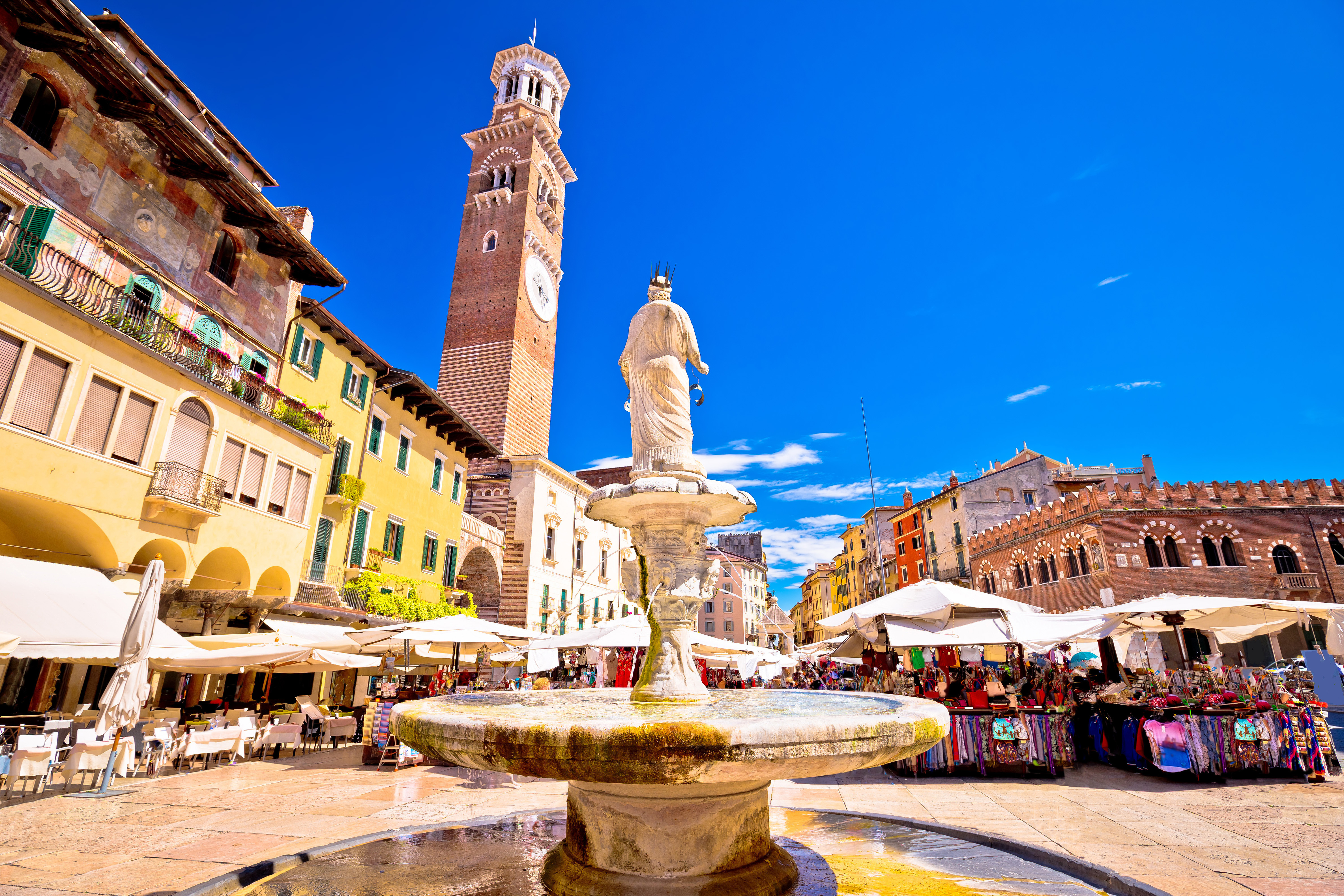 Det livlige Piazza delle Erbe i Verona med det høje Torre Lamberti og farverige bygninger, et populært turistmål i Norditalien