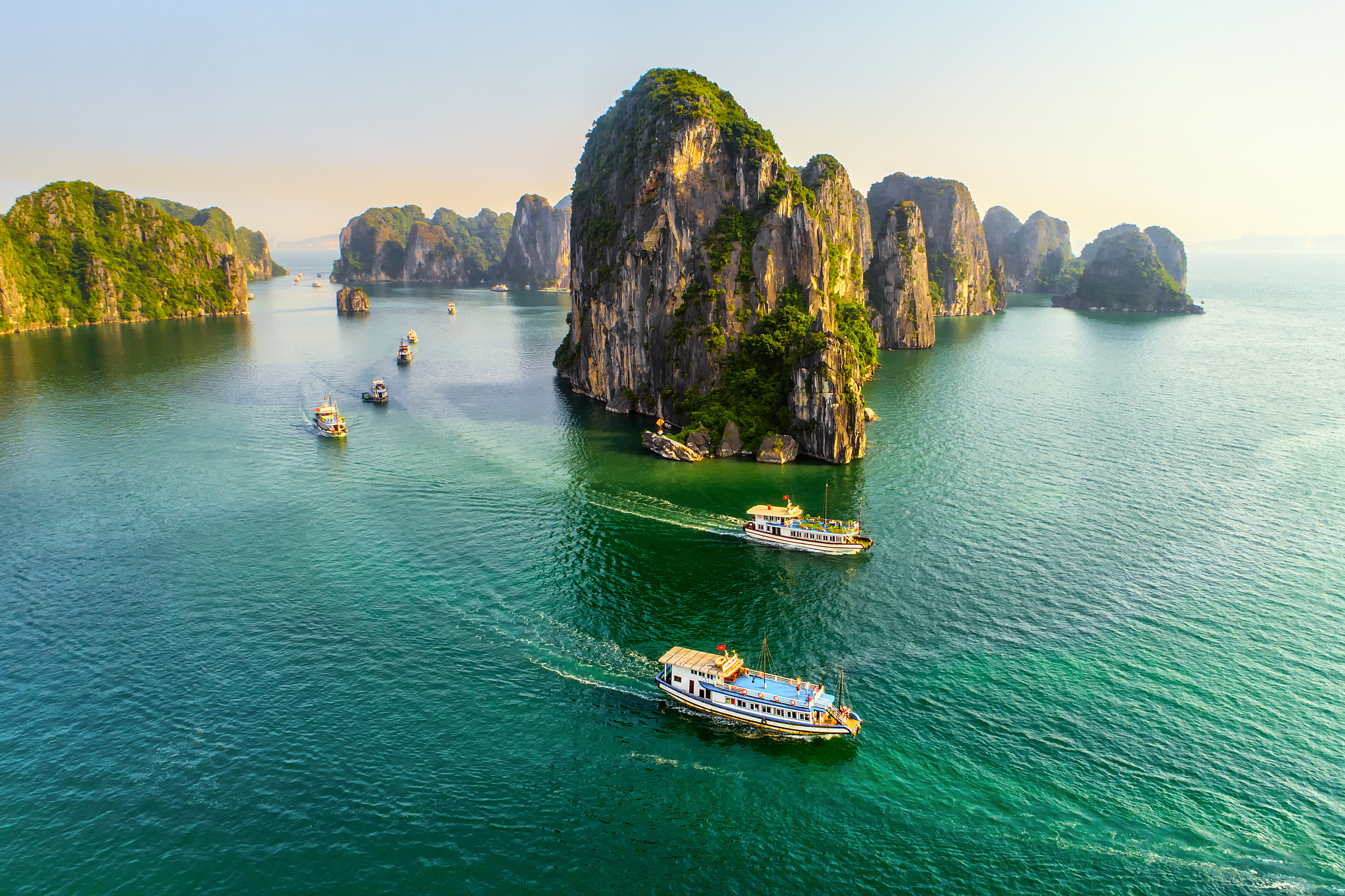 Majestætiske kalkstensformationer i Halong Bay Vietnam med cruisebåde der navigerer gennem det krystalklare turkise vand