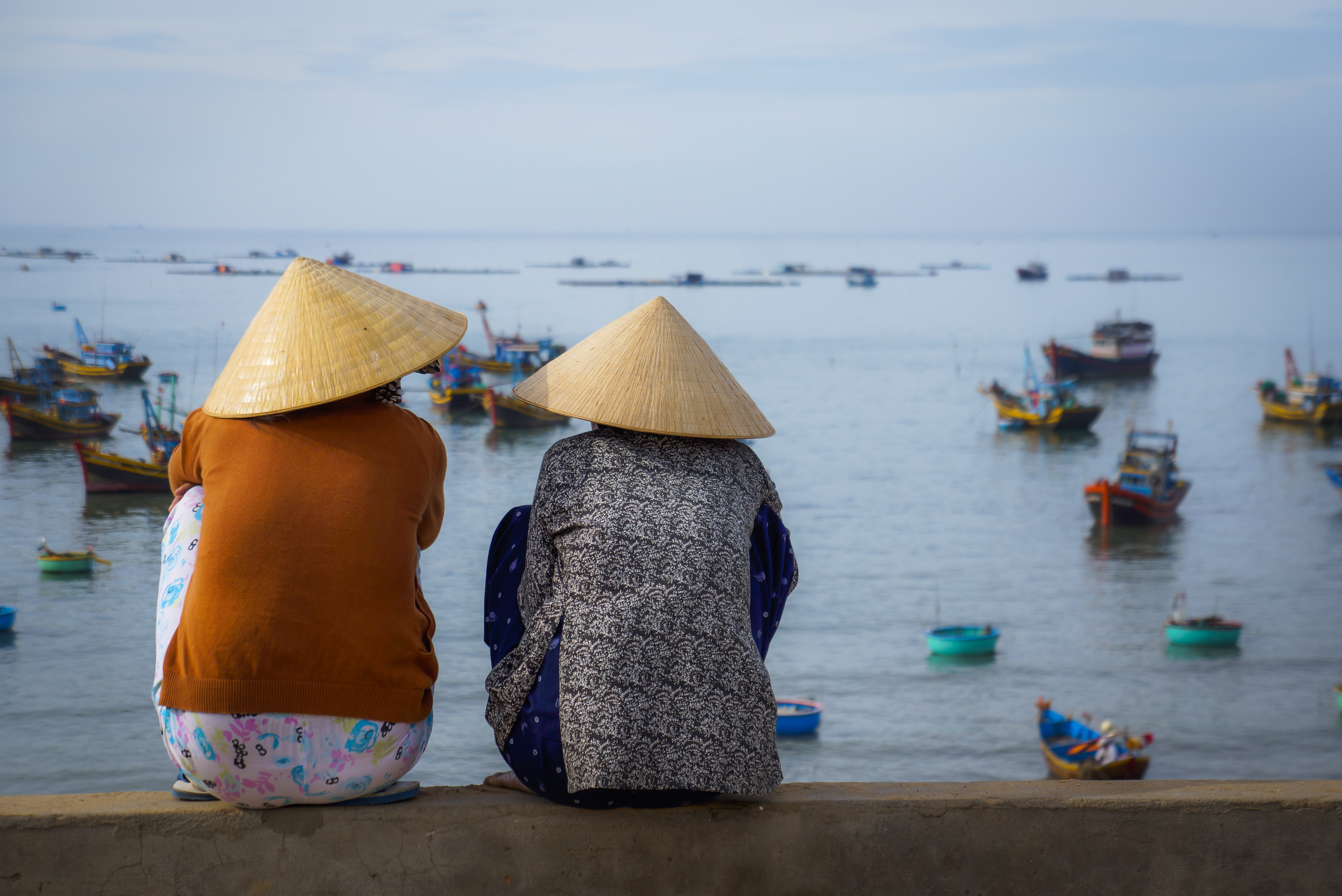 Stemningsfuldt billede af to vietnamesiske kvinder med traditionelle keglehatte ved fiskerihavnen i Mui Ne, Vietnam