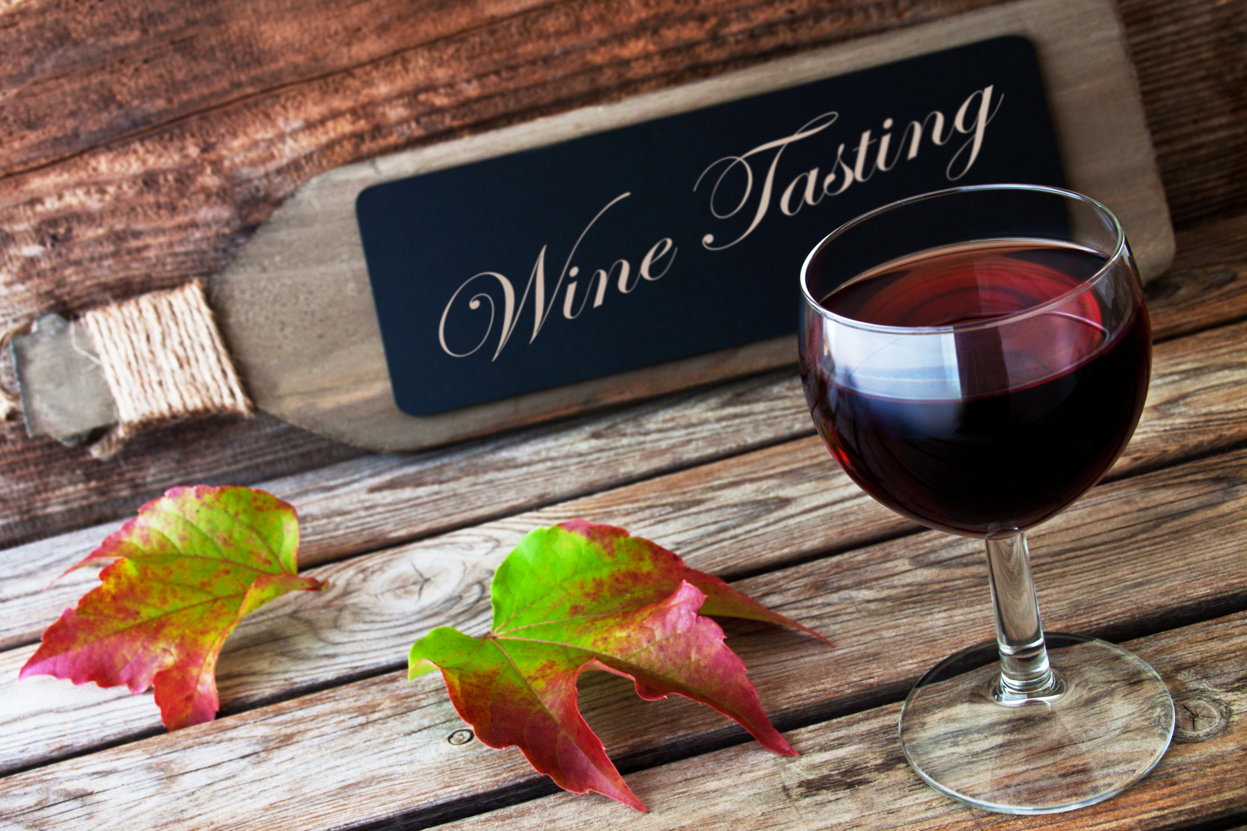 Autentisk vinsmagning med fyldt glas rødvin, efterårsblade fra vinstok og håndskrevet Wine Tasting skilt på rustikt træbord