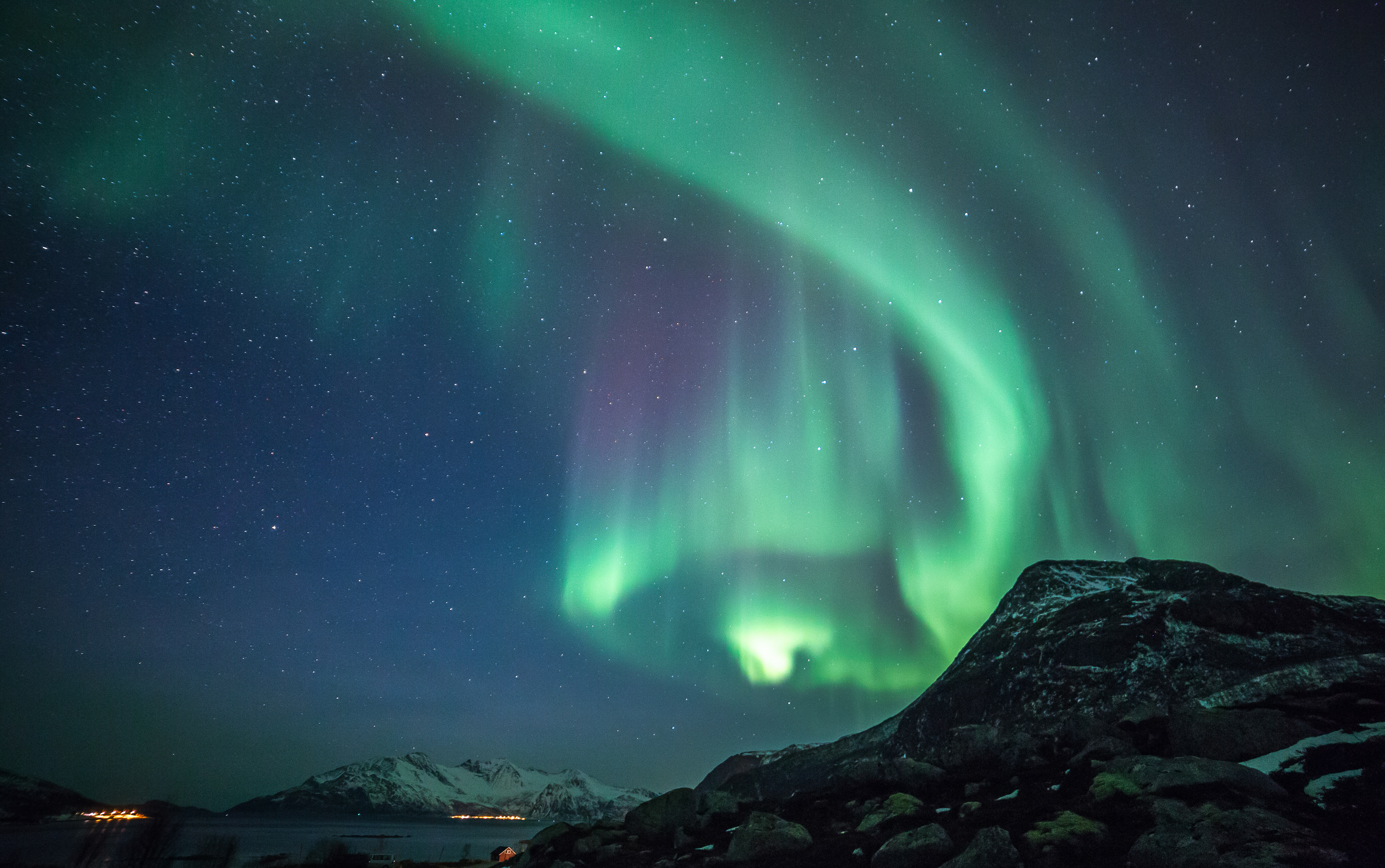 Utroligt nordlys fænomen med grønne lysslør over majestætiske norske bjerge i vinterlandskab