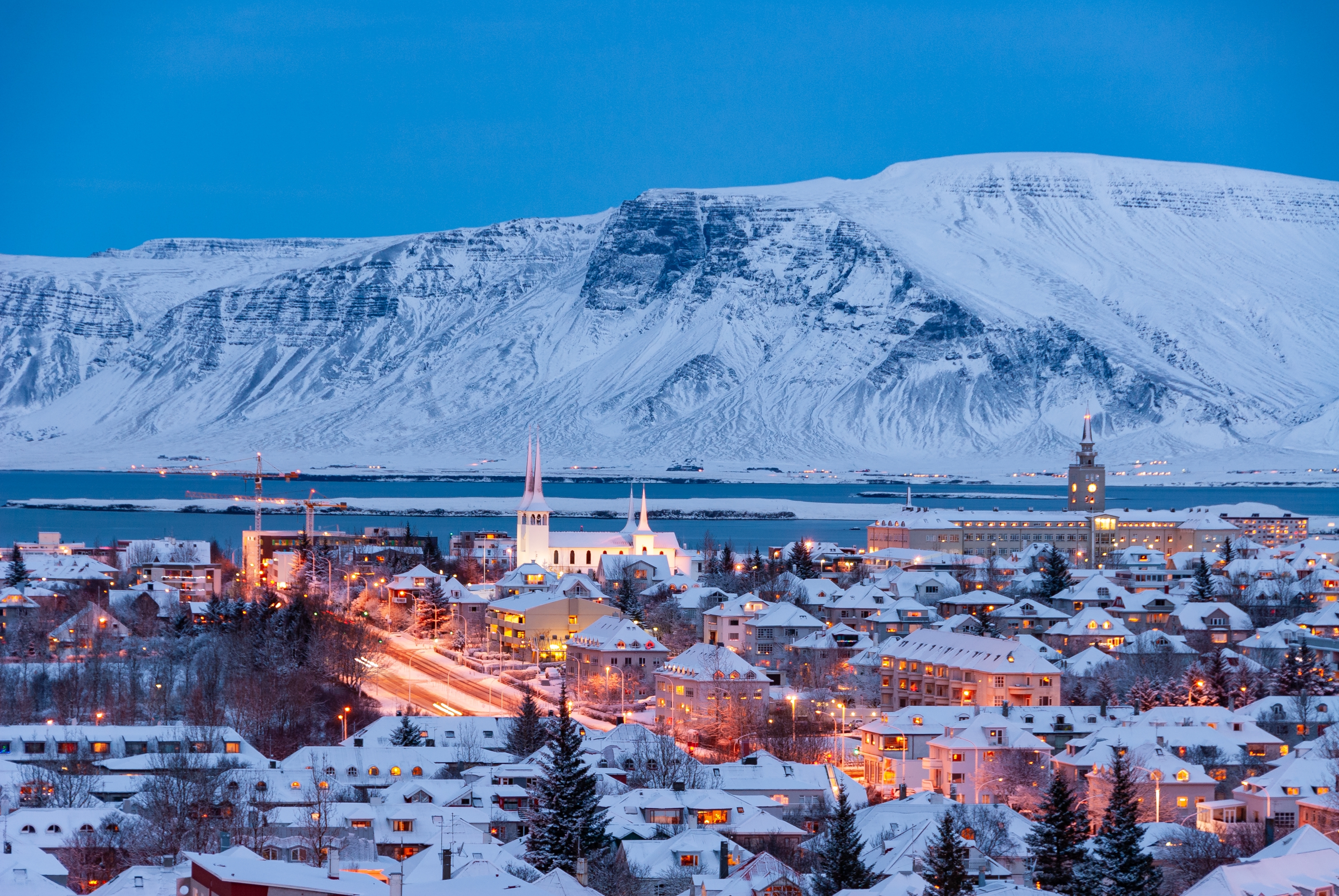 Betagende vinterstemning over Reykjavik ved aftenstid med oplyst bycentrum, Hallgrimskirkja og den smukke islandske natur i baggrunden