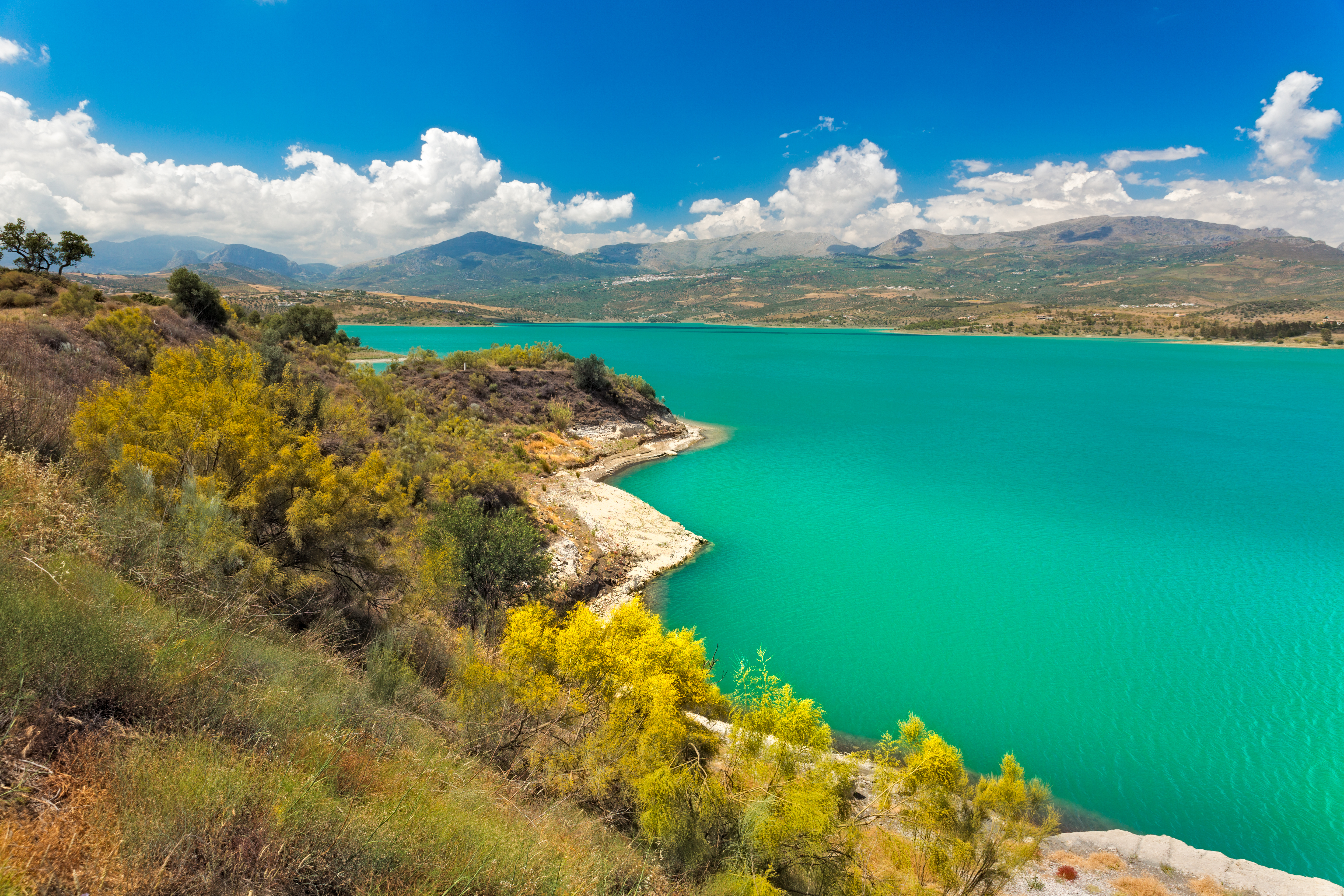 Turkisfarvet Lake Vinuela i Andalusien omgivet af gul vegetation og høje bjerge under blå himmel