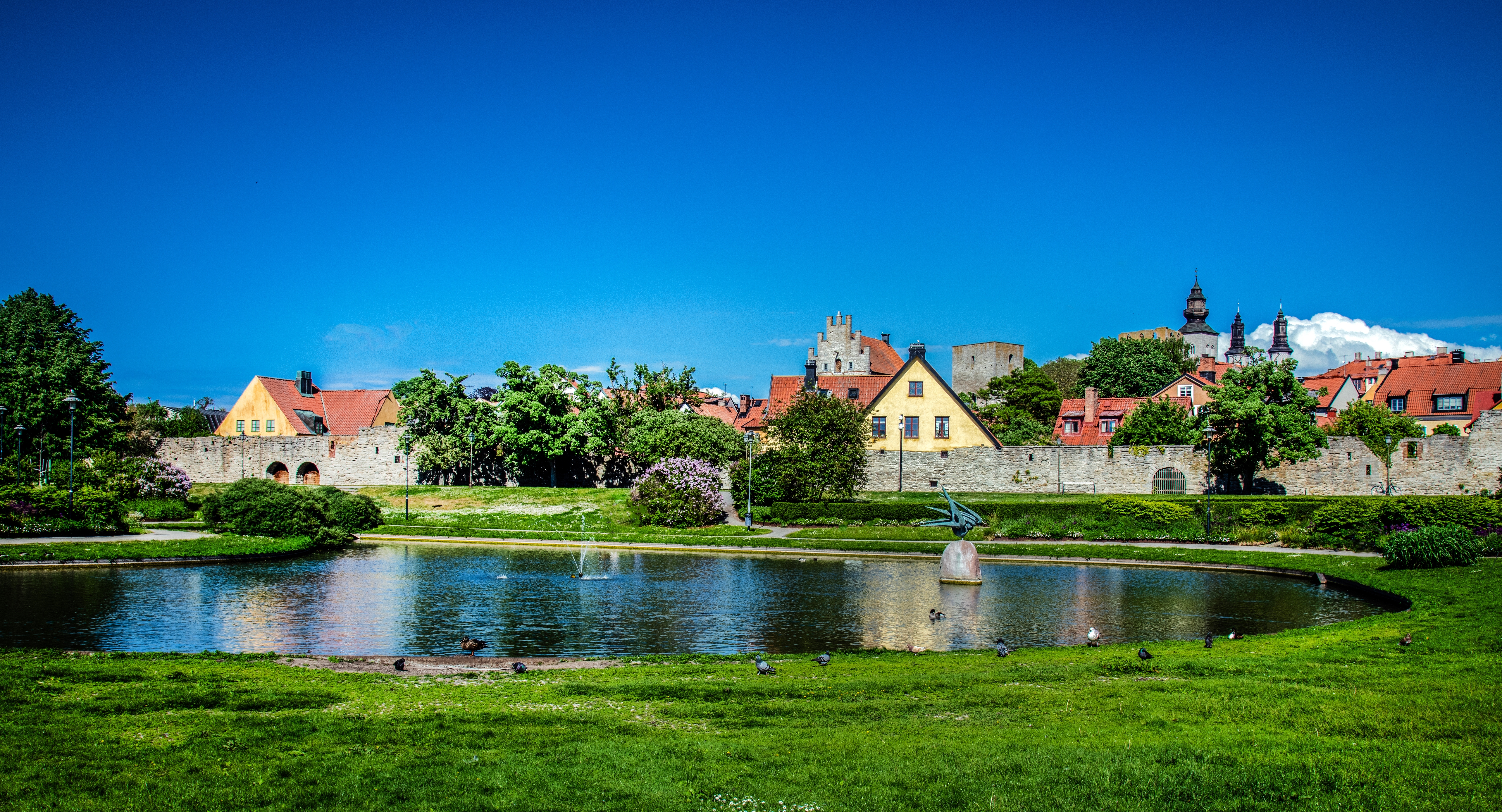Skøn sommerudsigt over det rekreative område Almedalen i Visby med historiske bygninger og mennesker, der nyder det gode vejr
