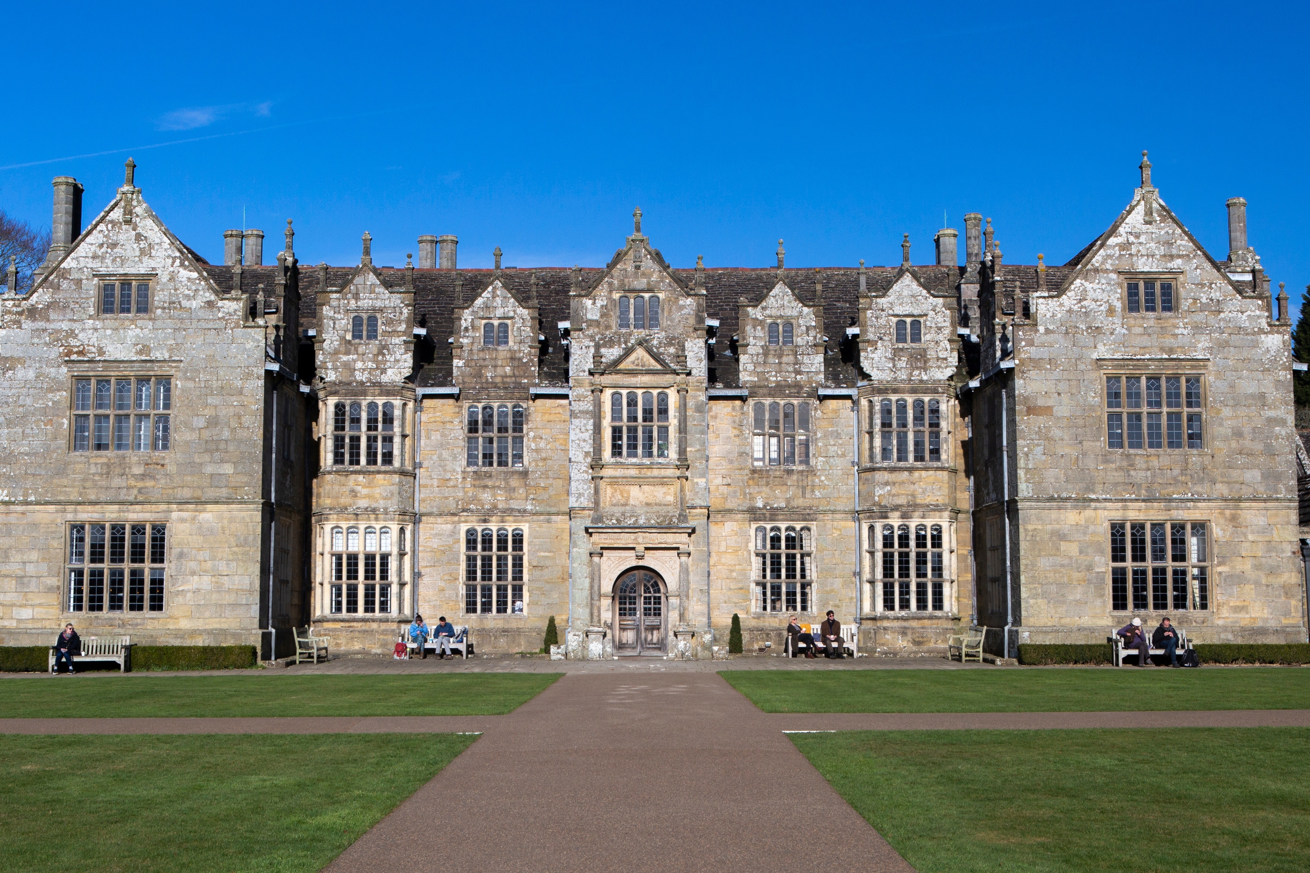 Imponerende Wakehurst Place herregård i West Sussex, England, med grønne plæner og blå himmel – del af Kew Gardens