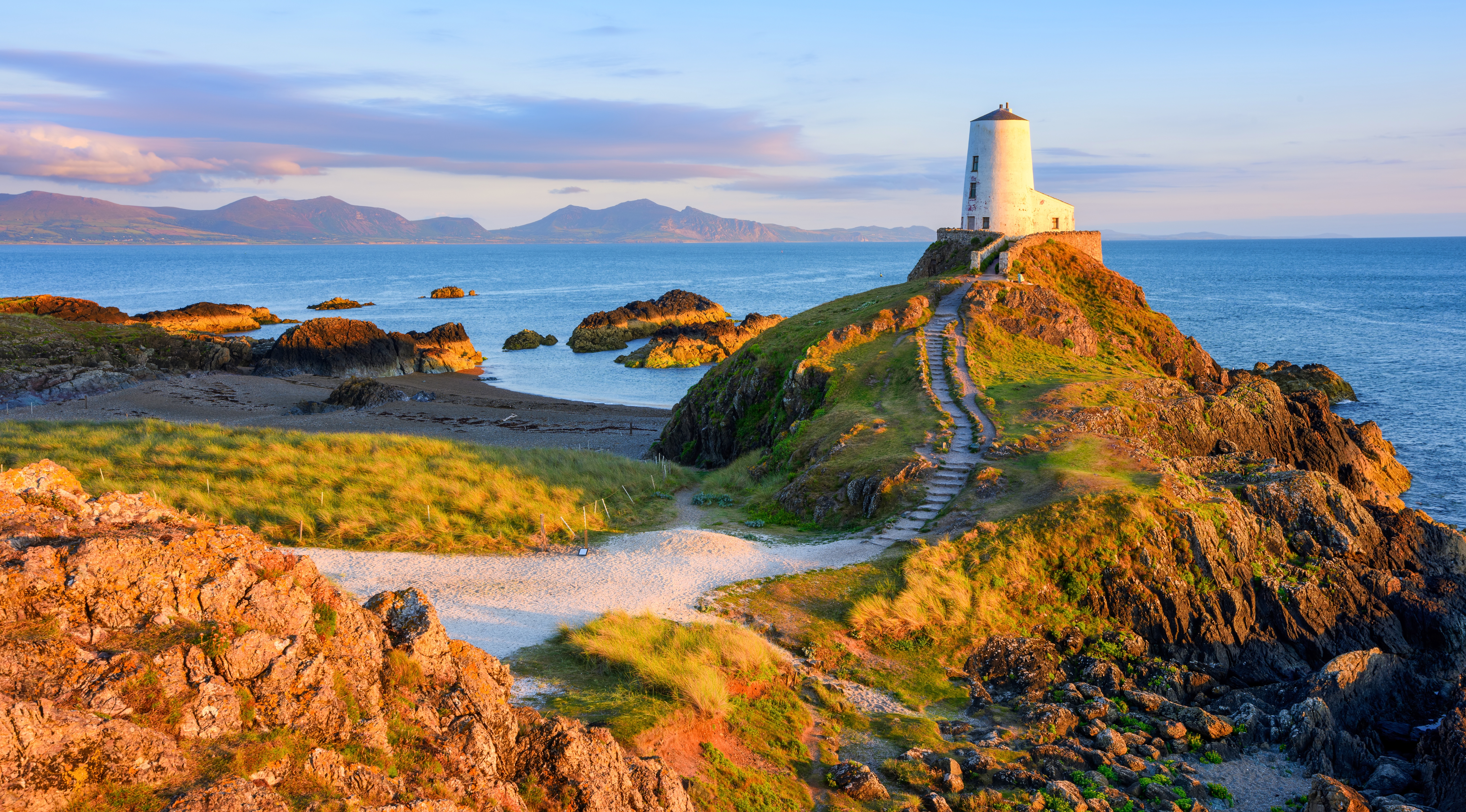 Malerisk fyrtårn på klippefyldt kyst ved Anglesey, Wales i gyldent lys