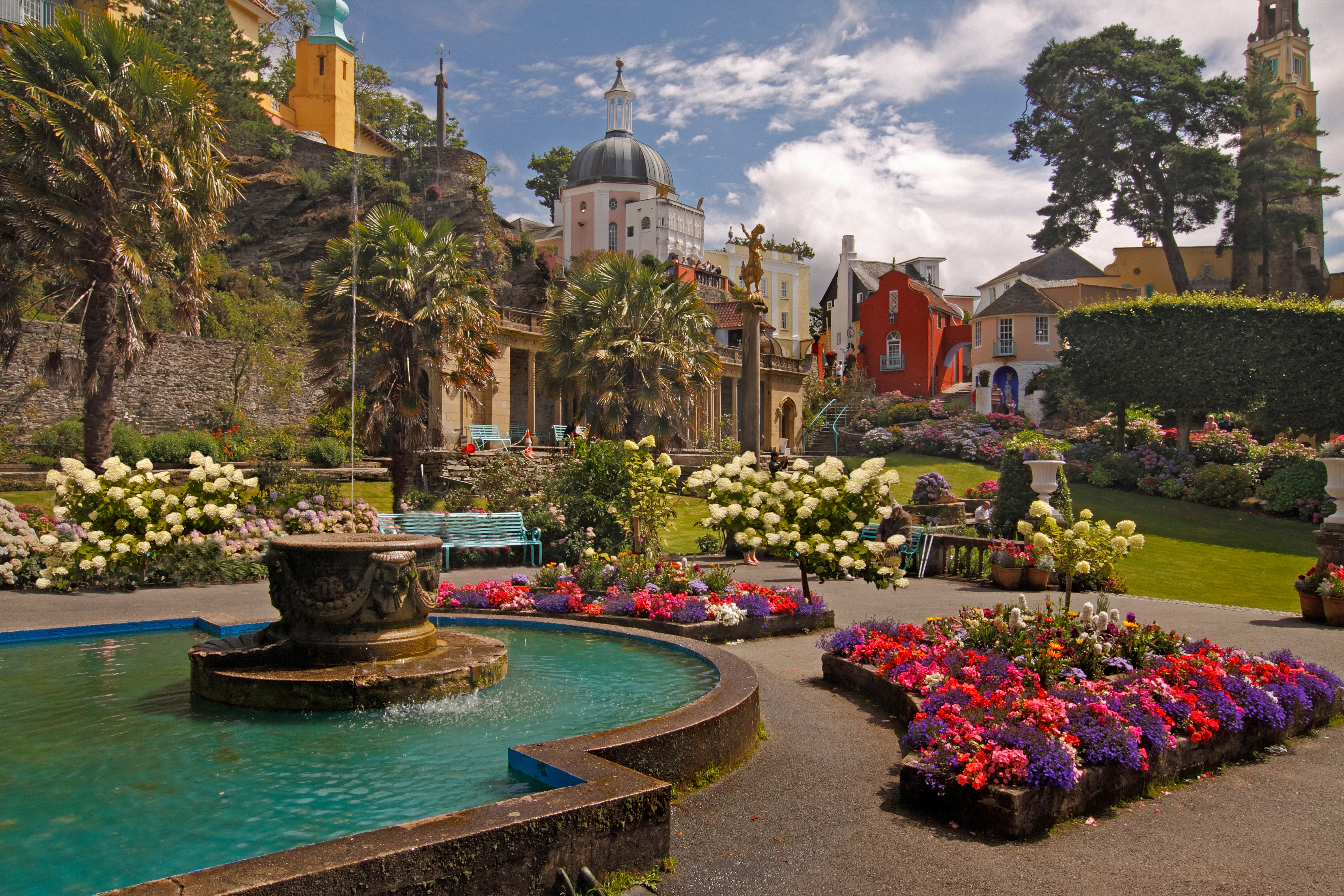 Maleriske Portmeirion i Wales med farverige bygninger i italiensk stil og velholdte blomsterhaver omkring en rund fontæne