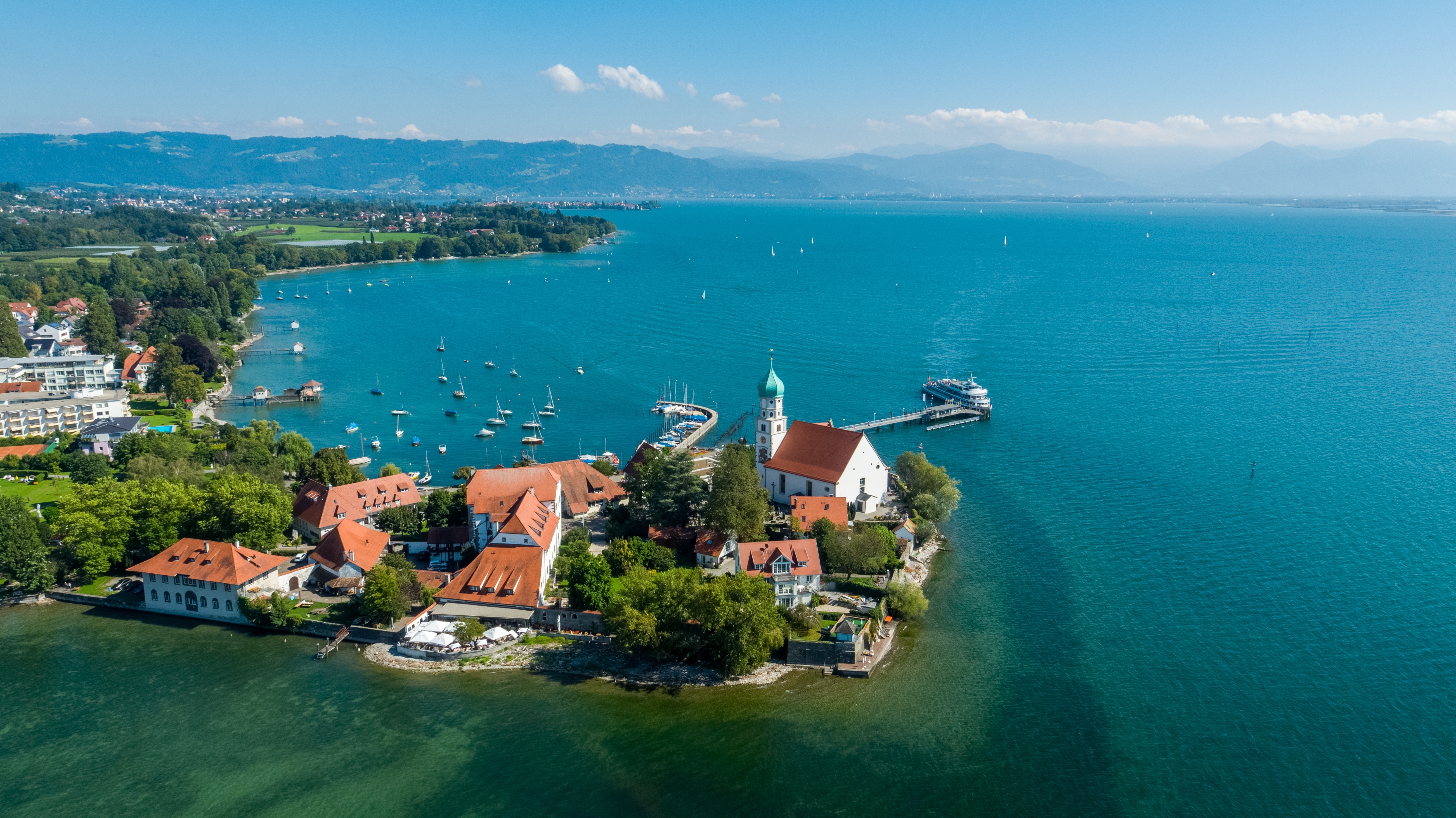 Panoramaudsigt over Wasserburg am Bodensee med den karakteristiske kirke og marina omgivet af det smukke turkisblå vand i Bodensø, Tyskland