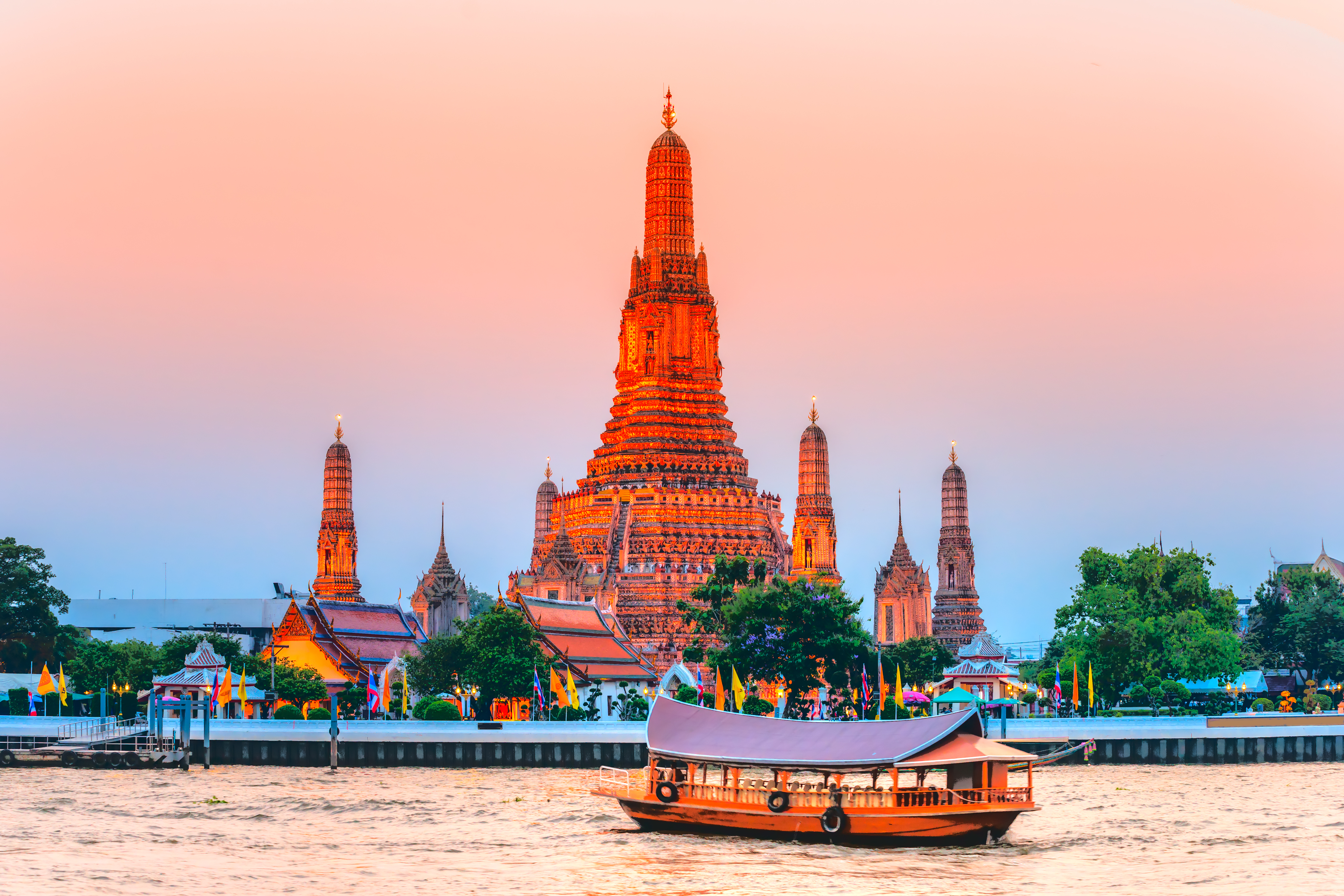 Wat Arun tempel Bangkok ved solnedgang med traditionel thai baad paa Chao Phraya floden