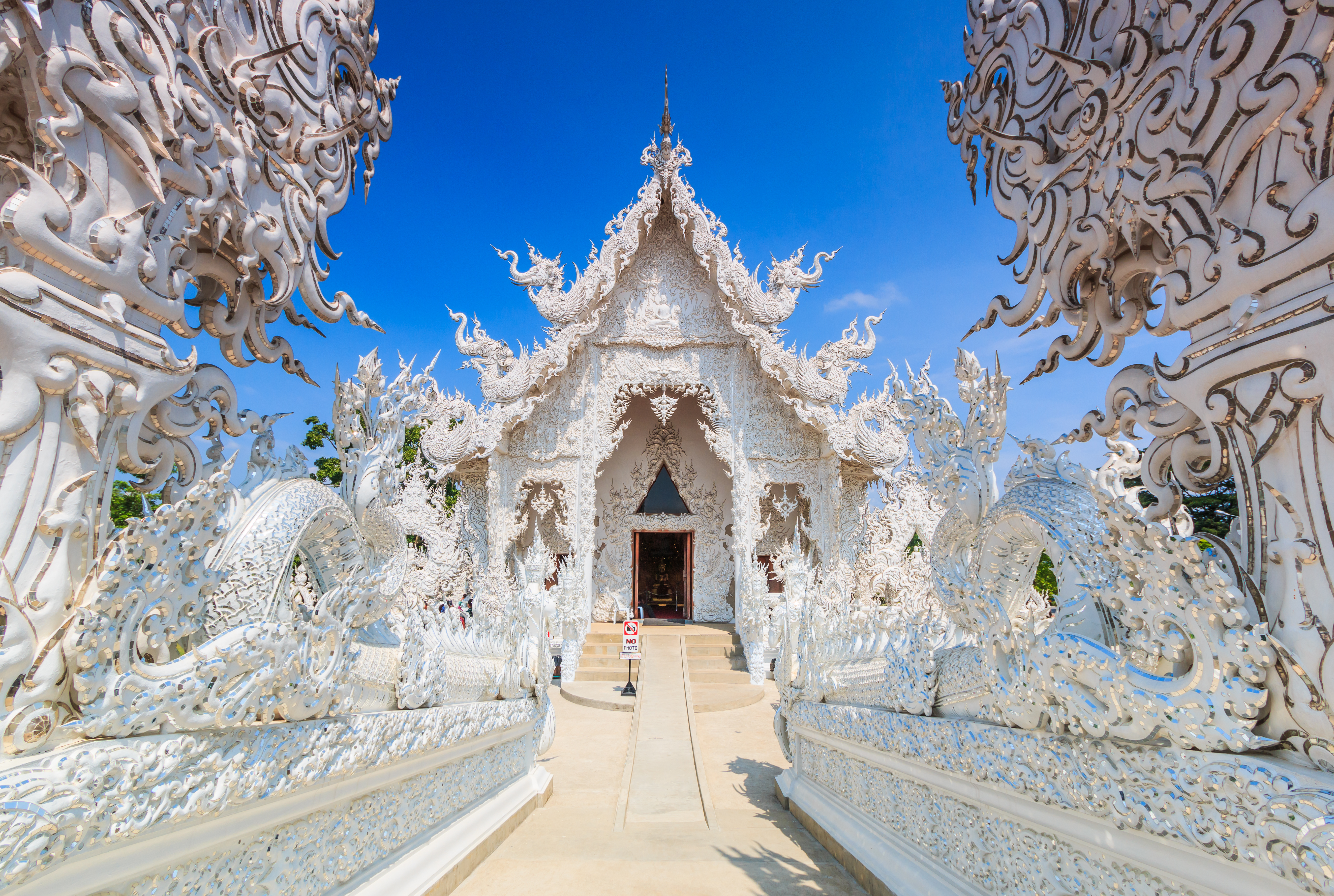 Imponerende hvidt tempel Wat Rong Khun i Chiang Rai, Thailand, med indviklede hvide ornamenter og kunstfærdige udskæringer langs indgangen