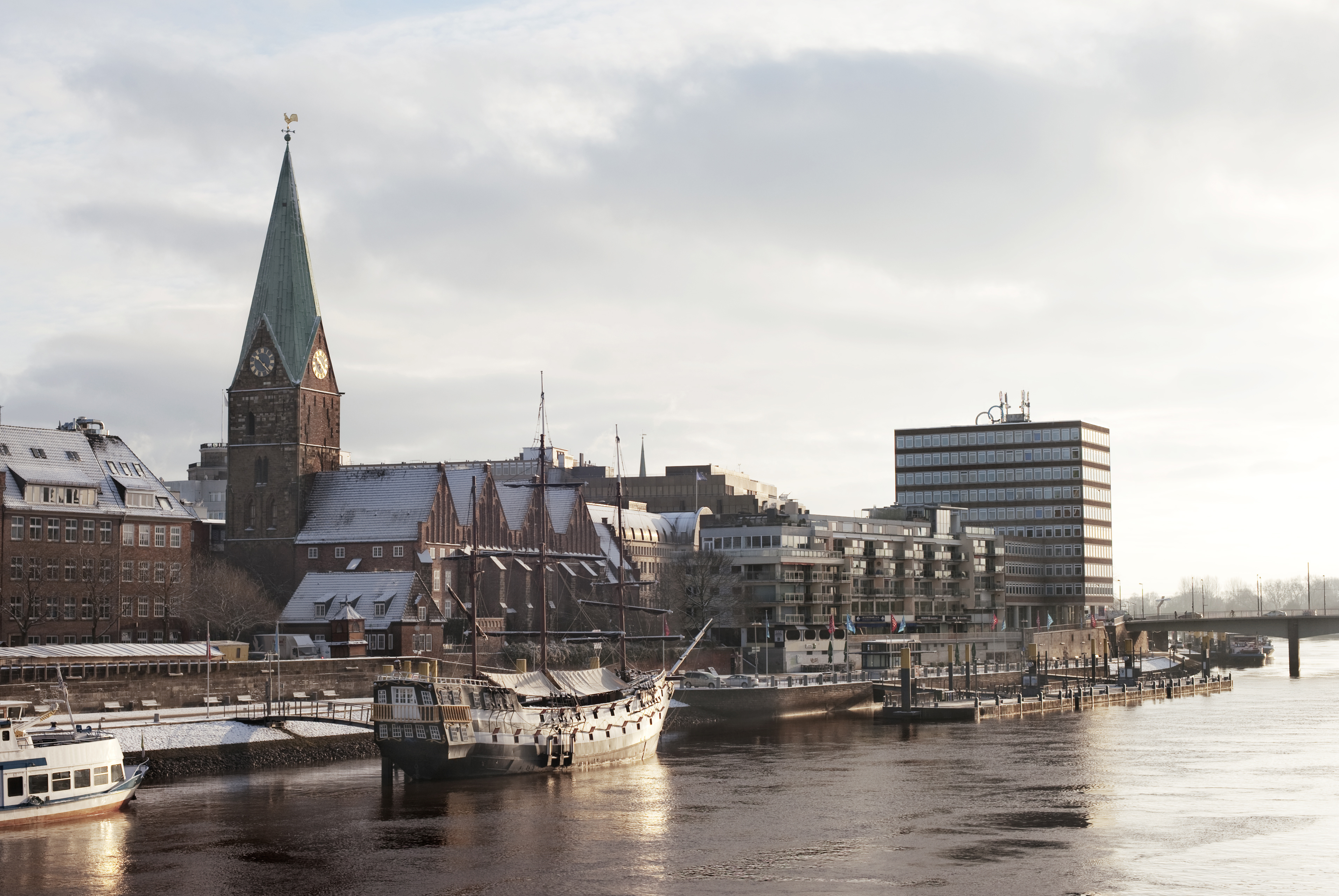Fantastisk vinterudsigt over Bremen ved solnedgang med byens karakteristiske tårne og historiske bygninger, der aftegner sig mod den gyldne himmel - en idyllisk scene med Weser-floden i forgrunden
