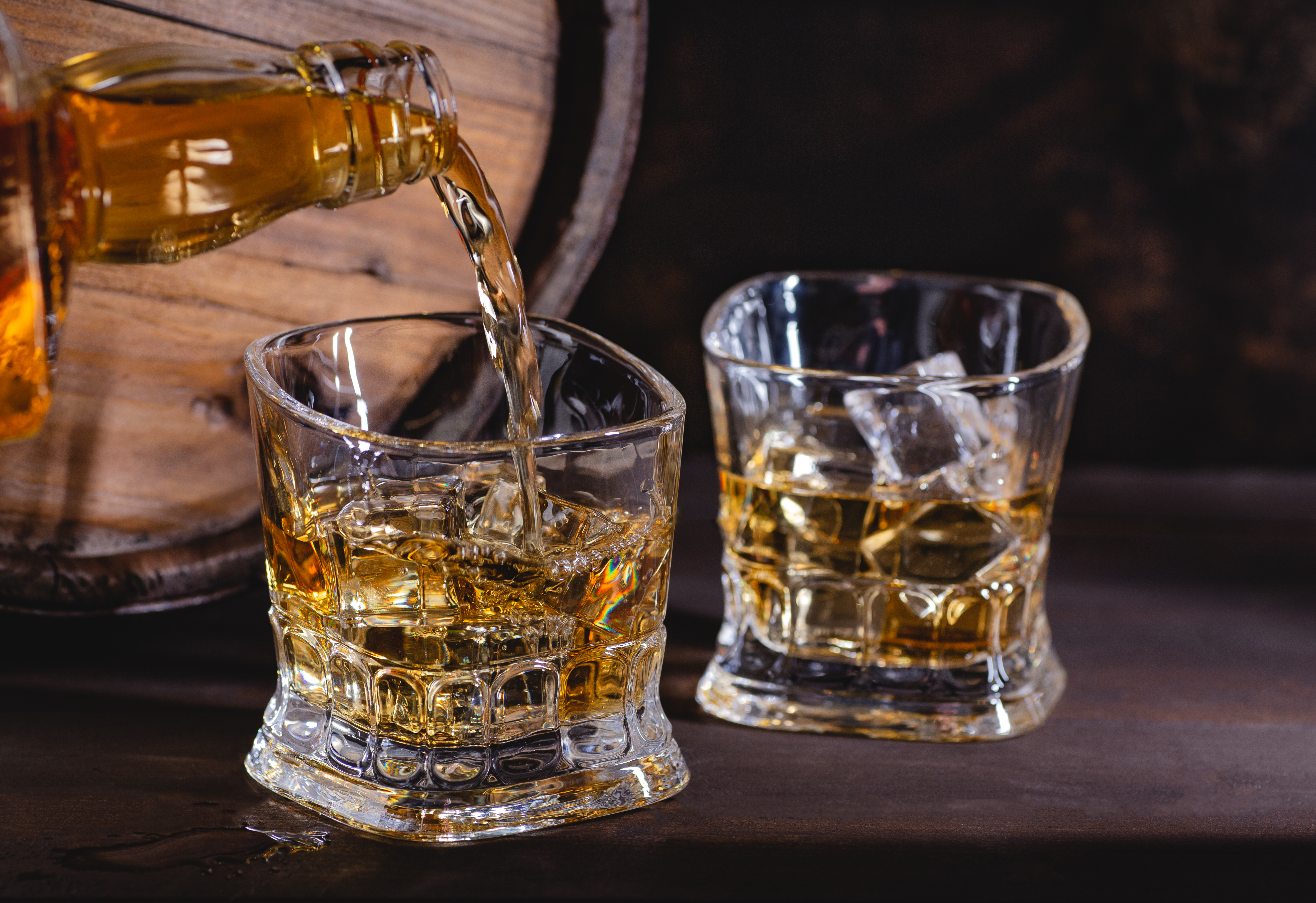 Lækkert nærbillede af en premium whiskey der hældes over isterninger i et stilfuldt cocktailglas på et mørkt træbord