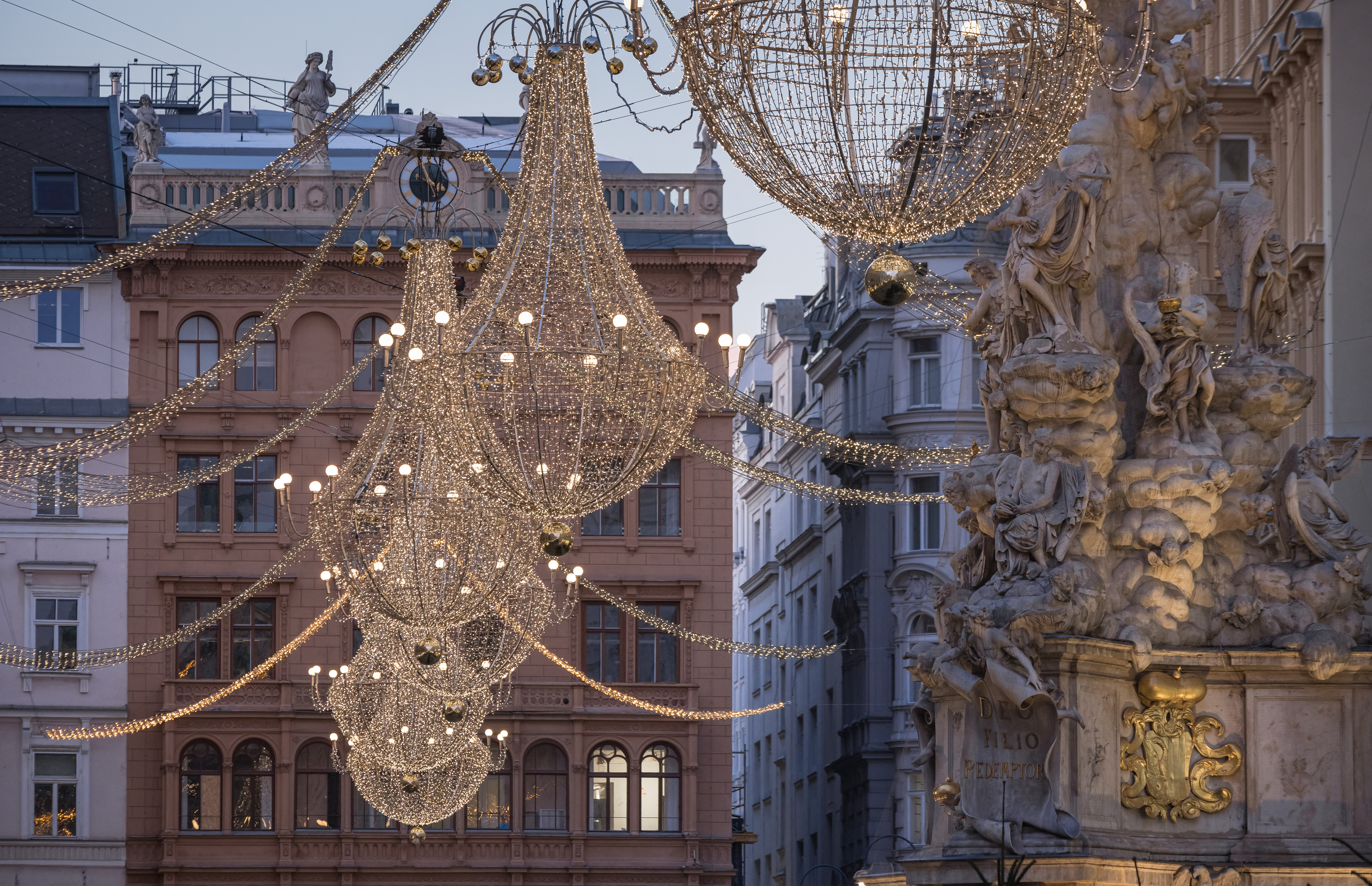 Pragtfulde lysekroner med tusindvis af julelys hænger over den historiske Graben-gade i Wien ved den ikoniske barokke pestsøjle
