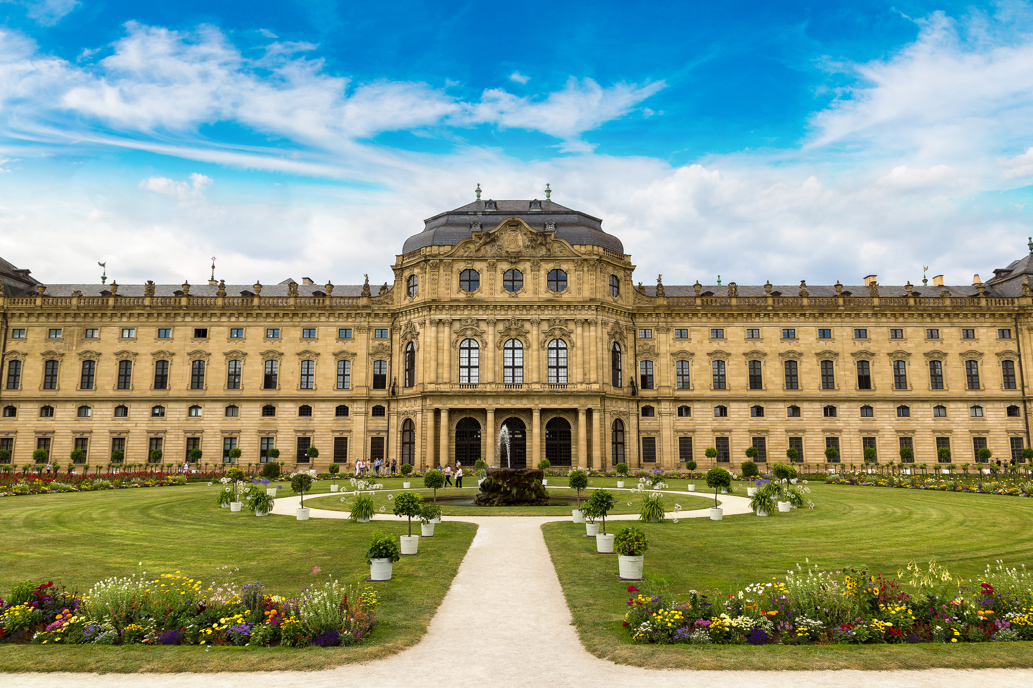 Udsigt til det berømte Würzburg Residenz palads i Bayern, Tyskland, med flot barokfacade, smuk have med blomster og springvand under en blå sommerhimmel